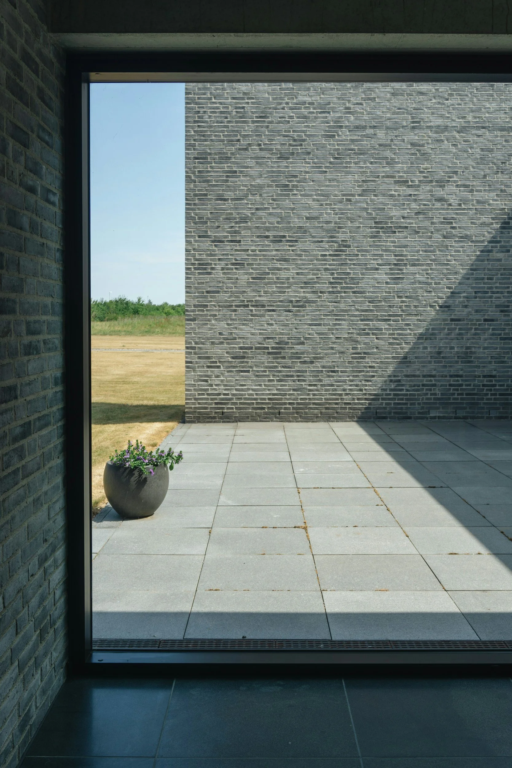 Dark brick-framed opening looking out to a stone-paved courtyard with open sky, illustrating the sightline and material mastery of Lindsey Architects' architectural design.