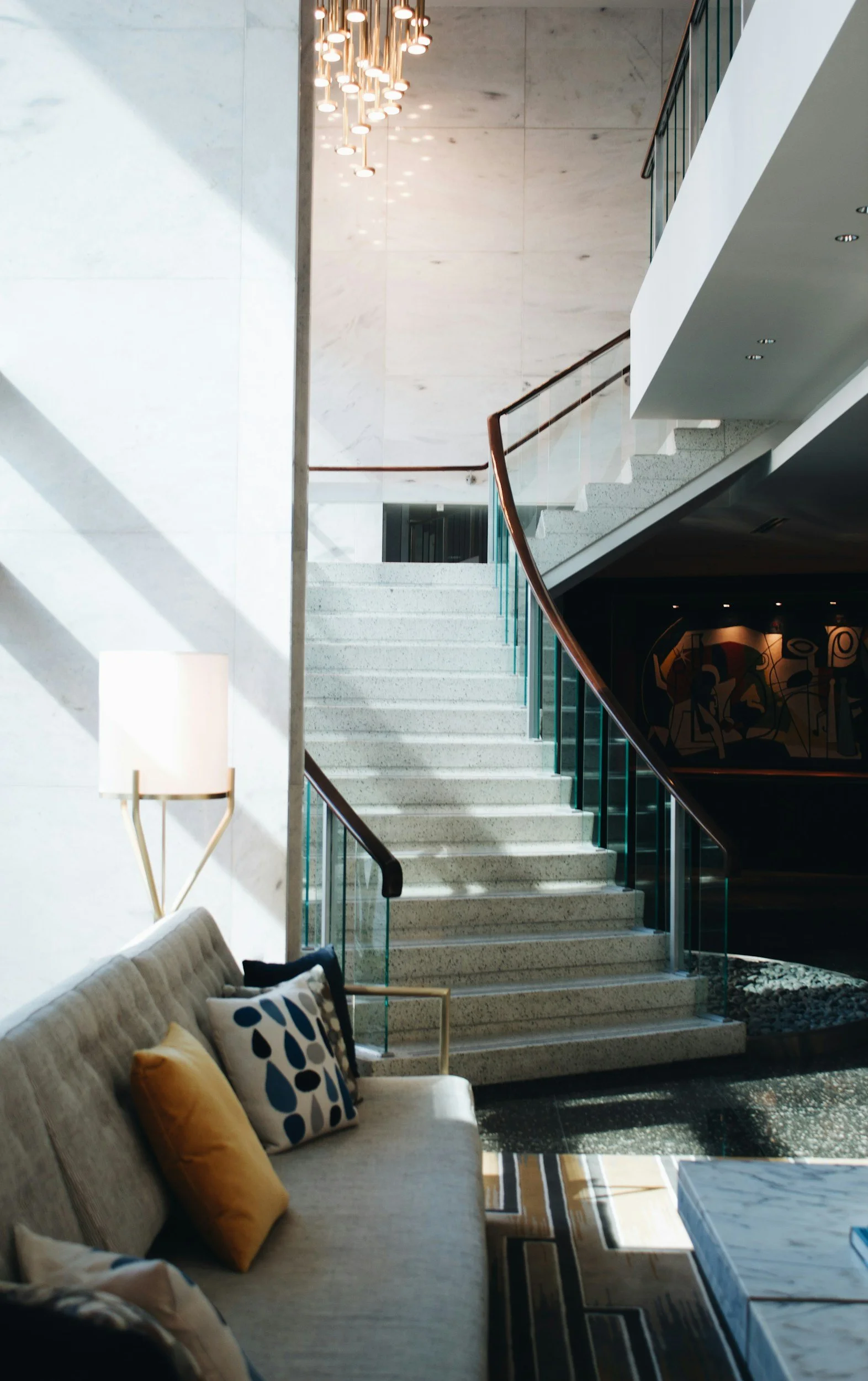 Dramatic modern staircase with stone treads, glass balustrade, timber handrail, and pendant chandelier in a custom home by Lindsey Architects in Portsmouth, NH.