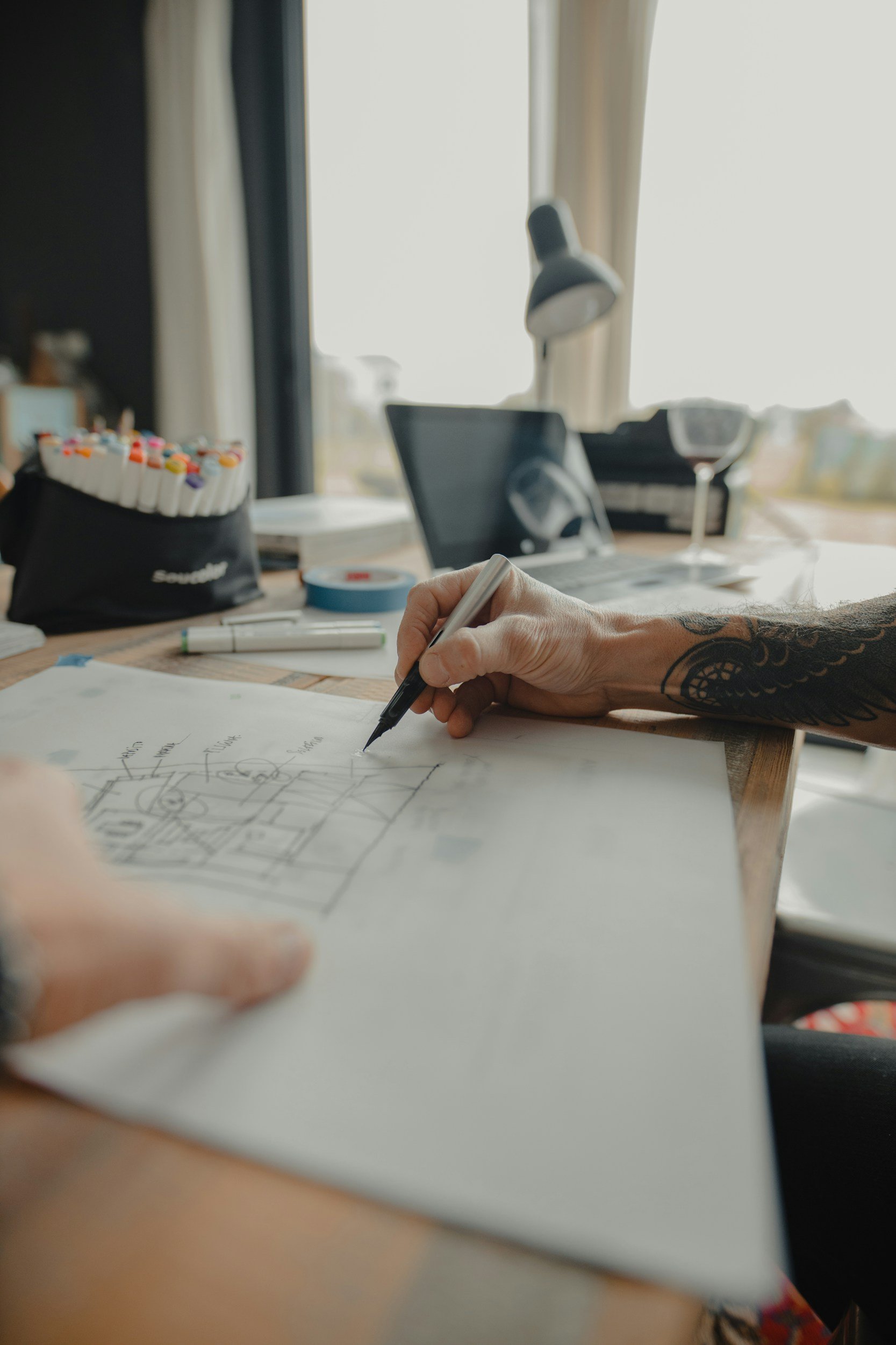A hand sketching architectural plans in pencil at a lit worktable — illustrating the vision-driven, meticulous planning approach Lindsey Architects uses for custom coastal homes in Portsmouth, New Hampshire.