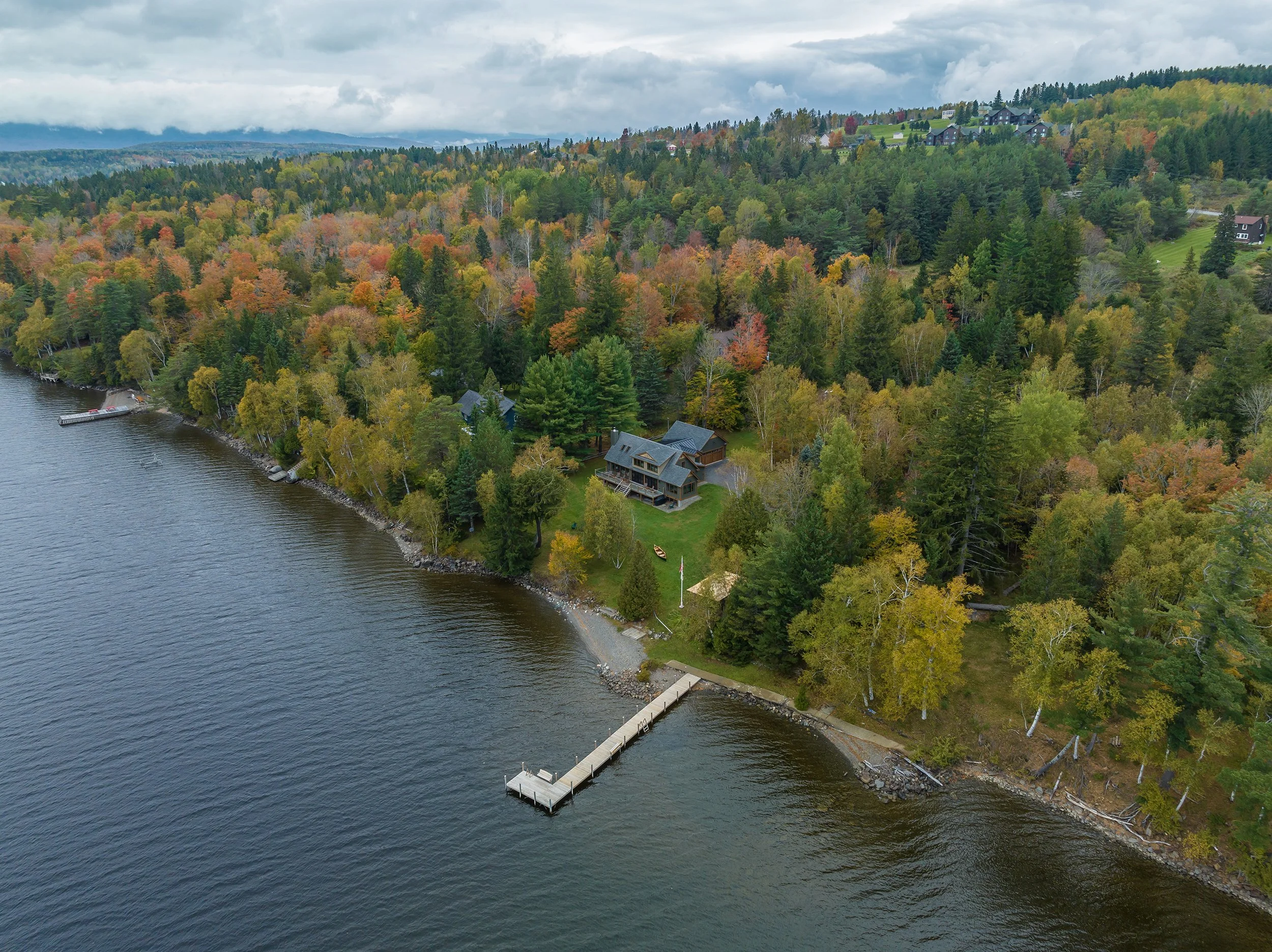 An aerial view of a custom lakeside retreat designed by Lindsey Architects, thoughtfully integrated into the natural Maine landscape with direct waterfront access, private dock, and expansive woodland surroundings. Nestled along the shoreline and sur