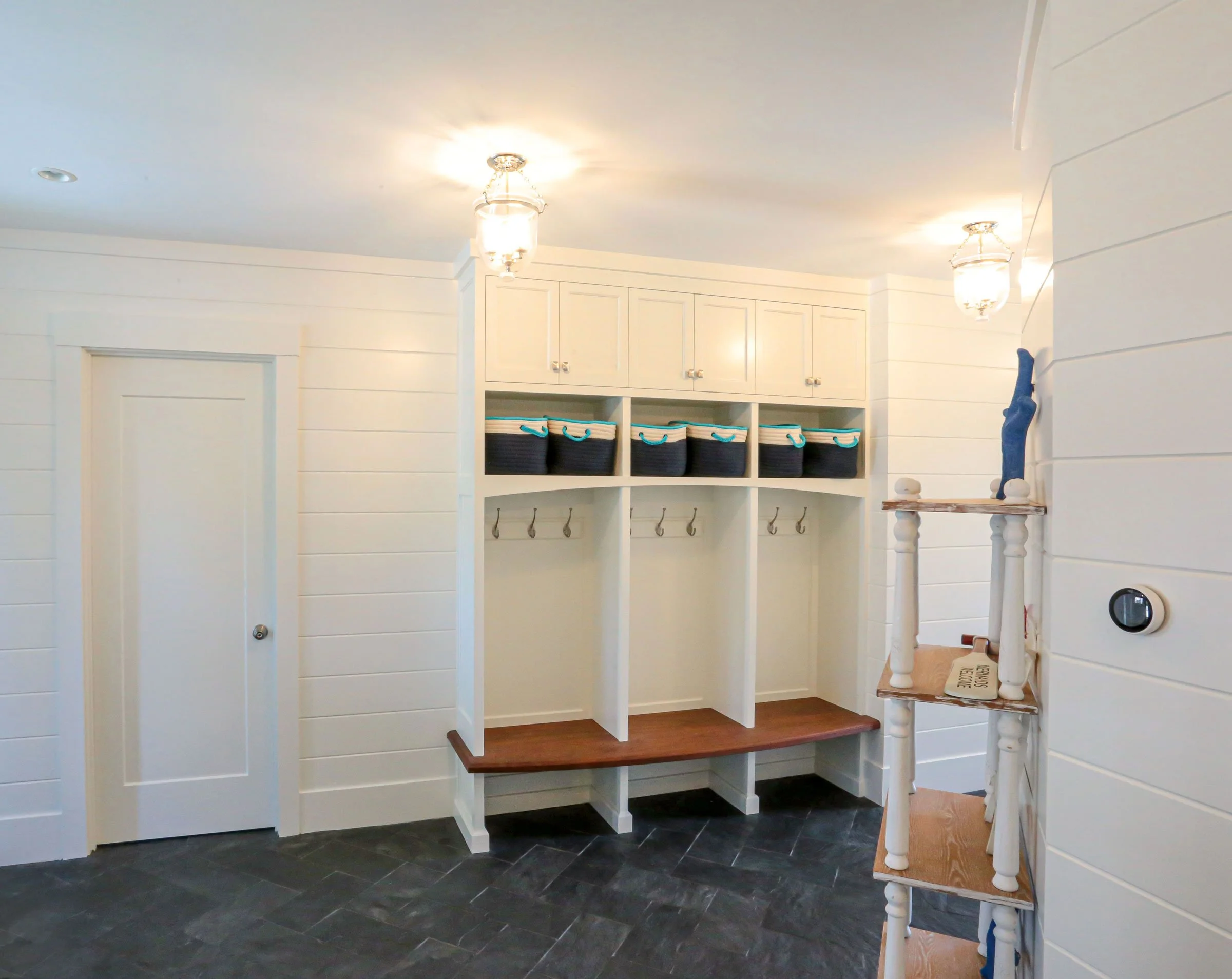 A bright and thoughtfully designed coastal mudroom by Lindsey Architects, featuring custom built-in storage cubbies, integrated bench seating, and timeless shiplap wall detailing inspired by New England waterfront living. Durable natural stone floori