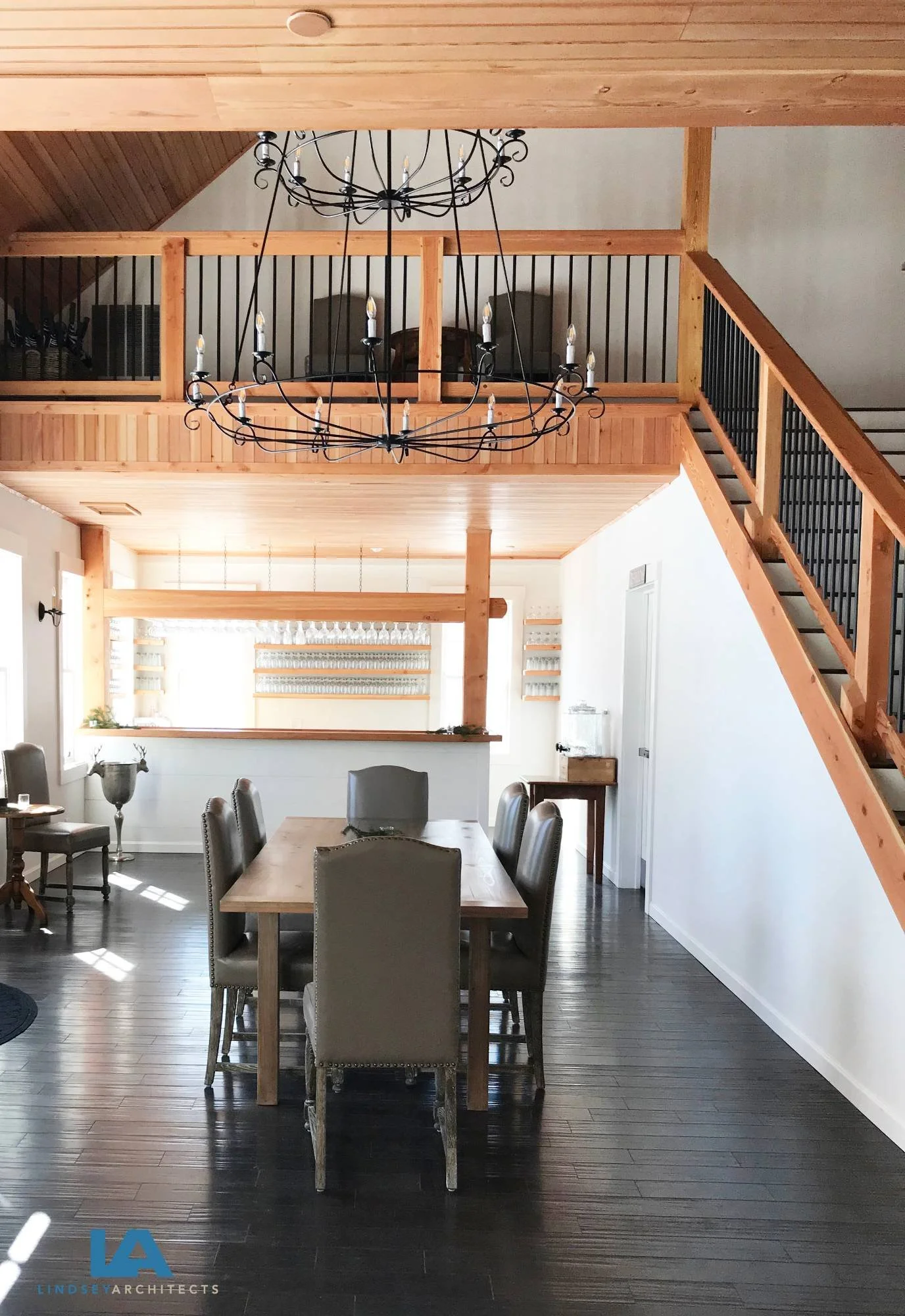 Beautifully restored historic timber-frame inn interior featuring a soaring vaulted wood-paneled ceiling, two-story open layout with a loft-level overlook and classic balustrade, large wrought iron chandelier, custom open staircase, farmhouse dining 