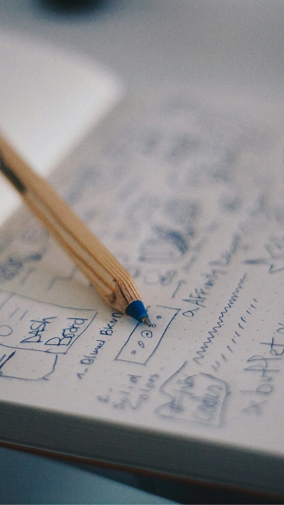 A pencil sketching a hand-drawn floor plan and room layout in a notebook — illustrating how Lindsey Architects translates initial ideas into buildable, bespoke custom home designs for clients in Rye, New Hampshire and the Seacoast.