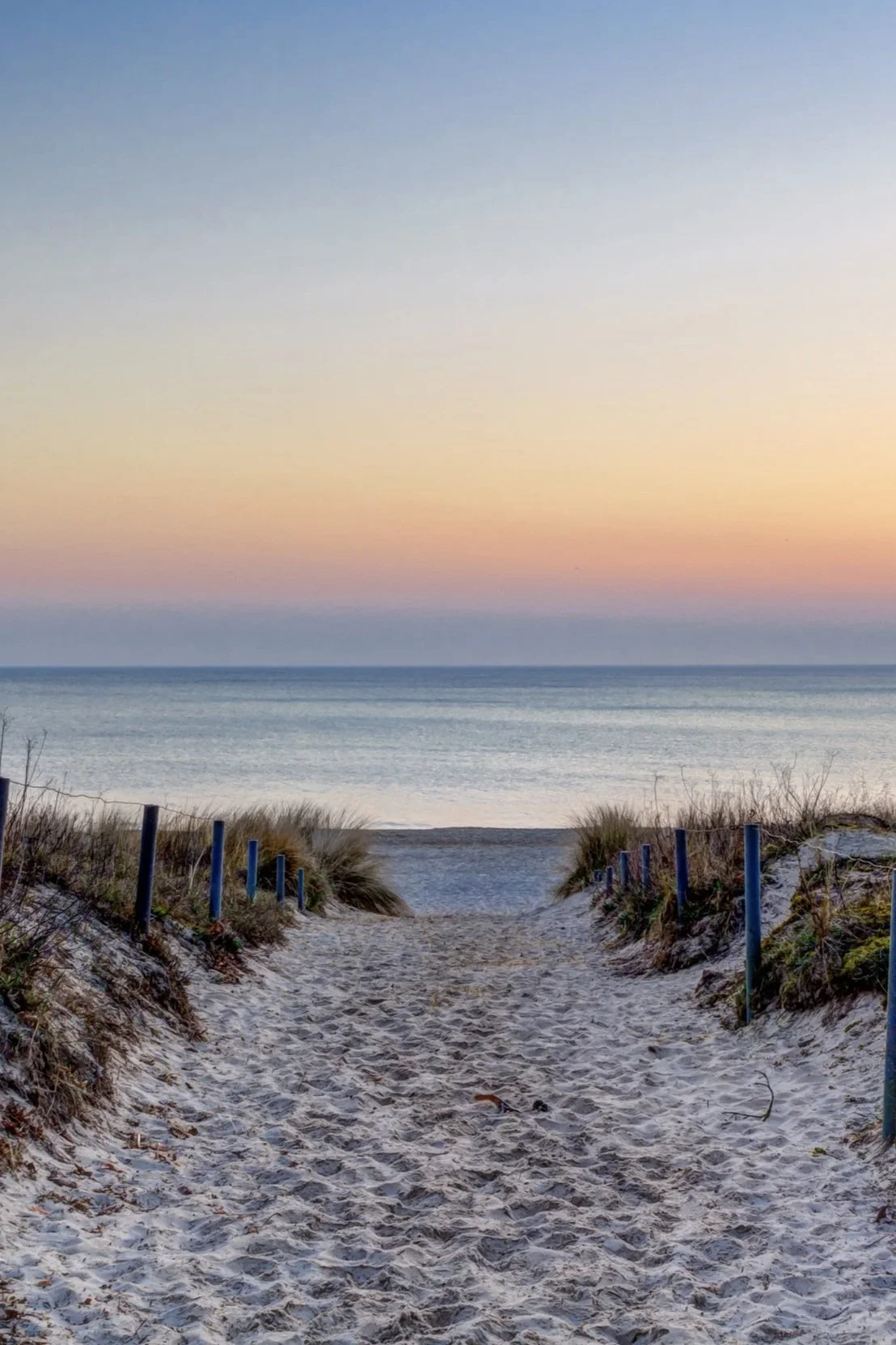Sandy beach path leading to the ocean at sunset along the Southern Maine coast, evoking the seamless flow Lindsey Architects designs into every coastal home.