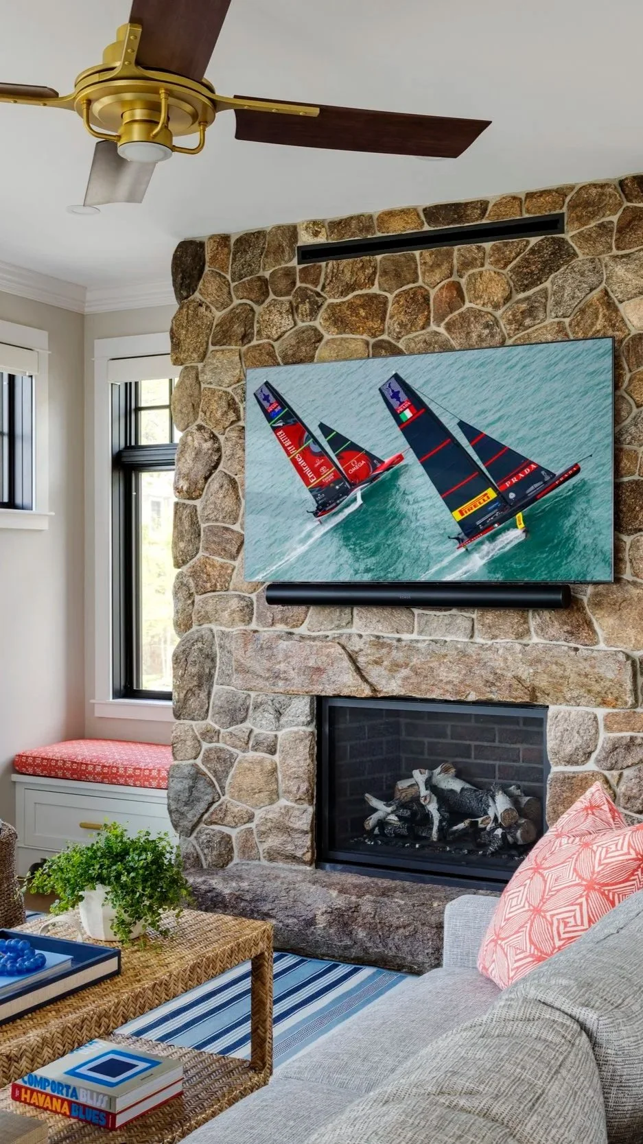 Fieldstone fireplace with a window seat and brass ceiling fan in a coastal Maine home, illustrating the classic natural materials Lindsey Architects uses for enduring design.