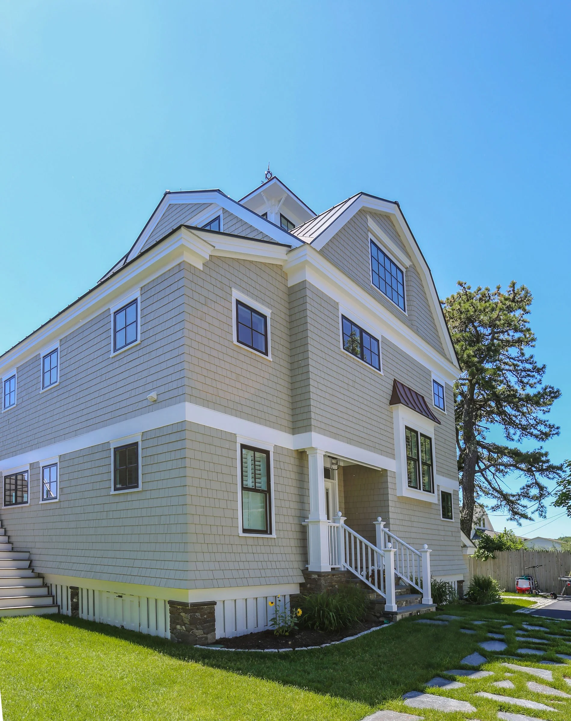 A timeless coastal residence designed by Lindsey Architects, featuring classic cedar shingle siding, layered rooflines, and elevated architectural detailing inspired by traditional New England waterfront homes. The carefully proportioned exterior, cu