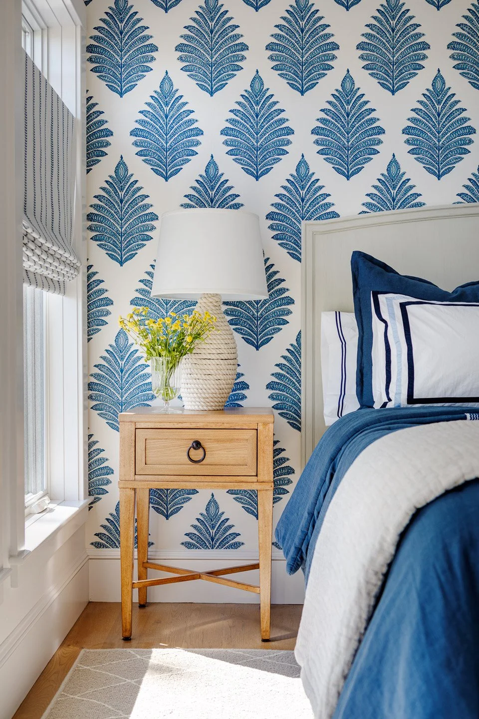 Lindsey Architects - Custom Residential A refined coastal bedroom detail designed by Lindsey Architects, featuring custom blue botanical wallpaper, layered textiles, and soft natural light inspired by the Maine coastline. Warm wood furnishings, tailo