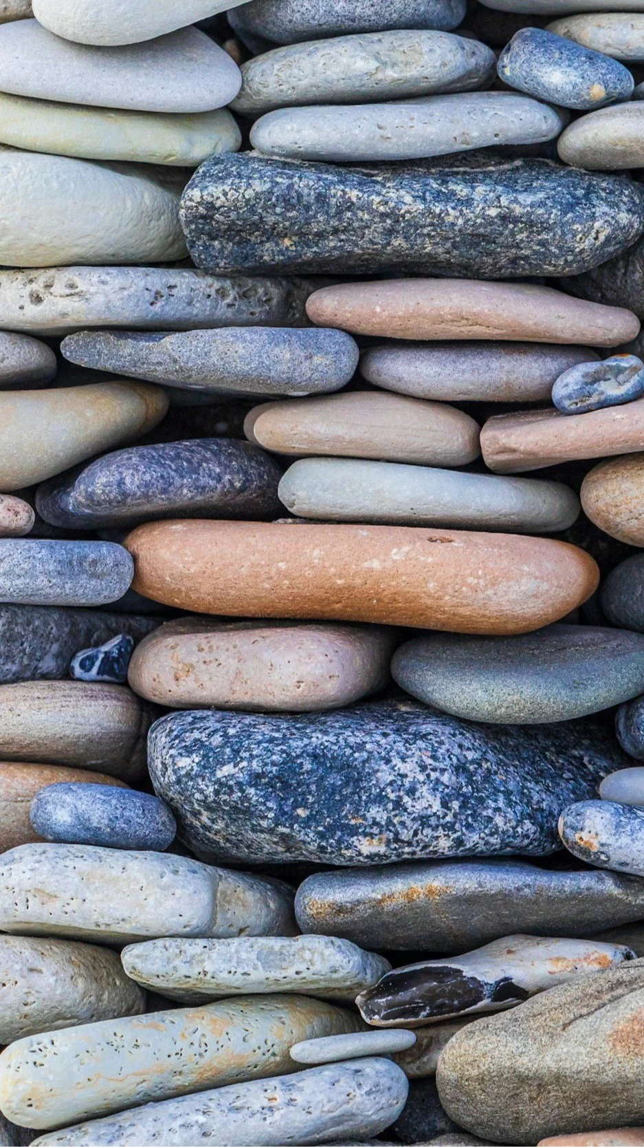Close-up of smooth, rounded river and beach stones in grey, blue, and warm tones — a coastal New England texture image accompanying Lindsey Architects' discussion of establishing trust and communication with your builder in custom home projects.