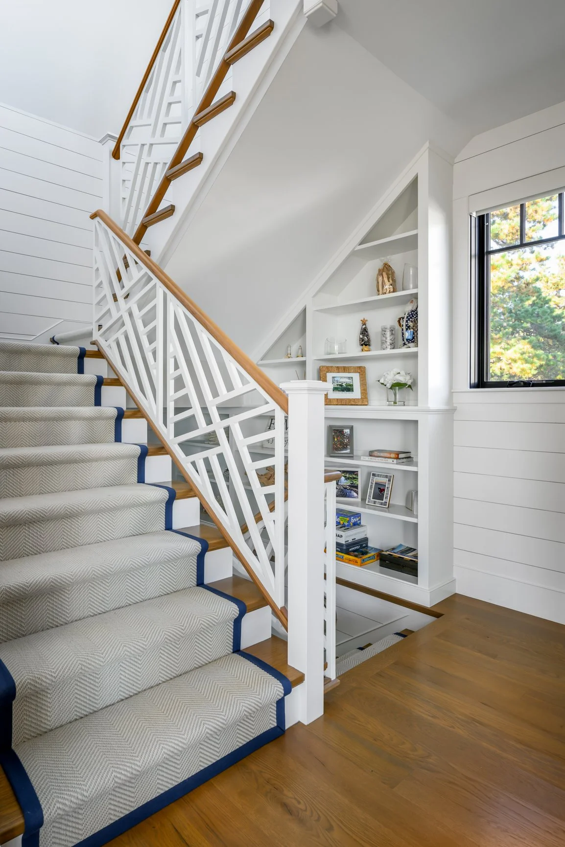 A custom staircase designed by Lindsey Architects, blending clean coastal detailing with timeless New England craftsmanship. White shiplap walls, warm oak flooring, and sculptural railing design create a bright and welcoming interior that balances el