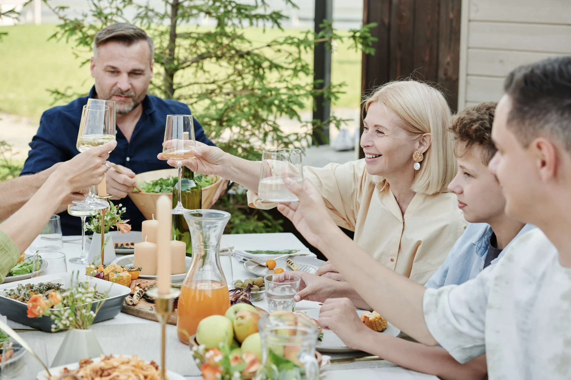 Multi-generational family gathered for an outdoor meal on a covered porch, raising a toast — illustrating how Lindsey Architects designs custom homes around the way families live and entertain in coastal Maine and New Hampshire.