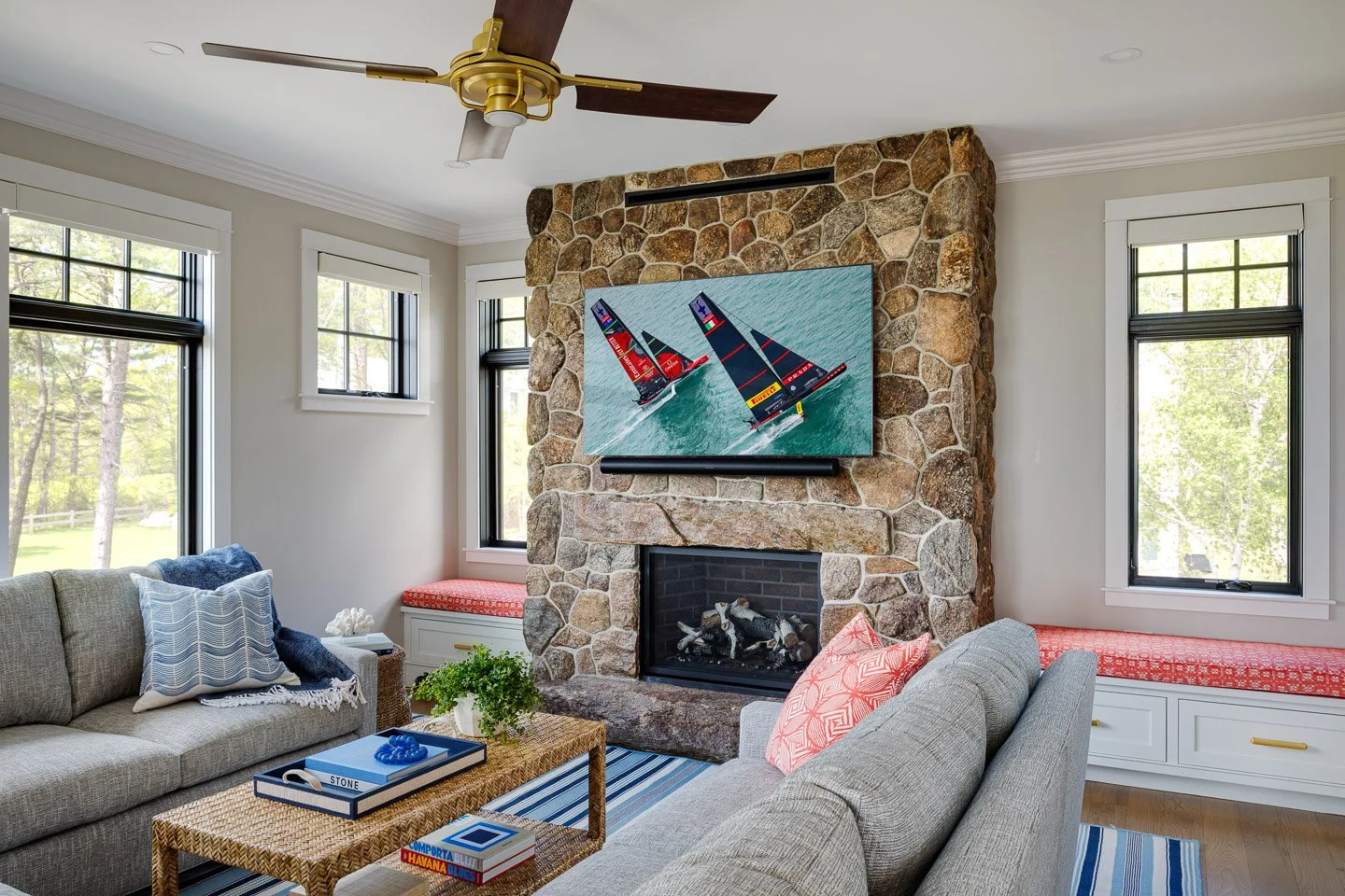 A warm and inviting coastal living room designed by Lindsey Architects, featuring a natural stone fireplace, custom built-in window seating, and refined contemporary New England detailing. Large windows, layered textures, and soft coastal-inspired fu