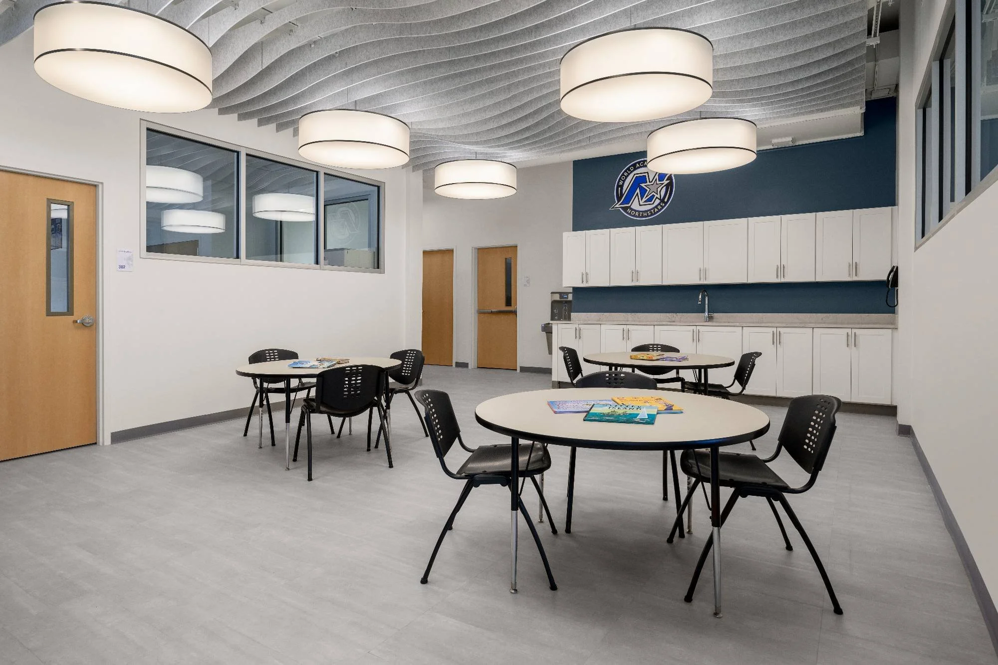Bright double-height school commons featuring a two-story window wall, tiered wood bench seating, and modern pendant lighting — private school addition in Nashua, NH by Lindsey Architects, serving Maine, NH, and MA.