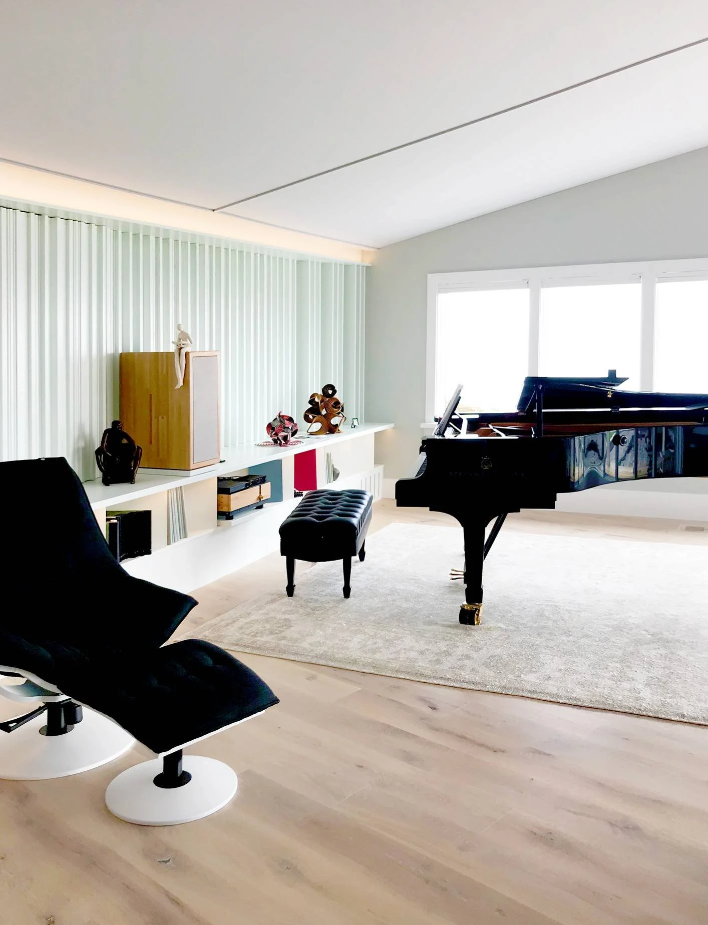 Modern coastal music and lounge room featuring a vaulted ceiling, wide-plank white oak flooring, a grand piano, sleek black modern lounge chairs, a low-profile white media console, sheer floor-to-ceiling drapery, and abundant natural light — custom l