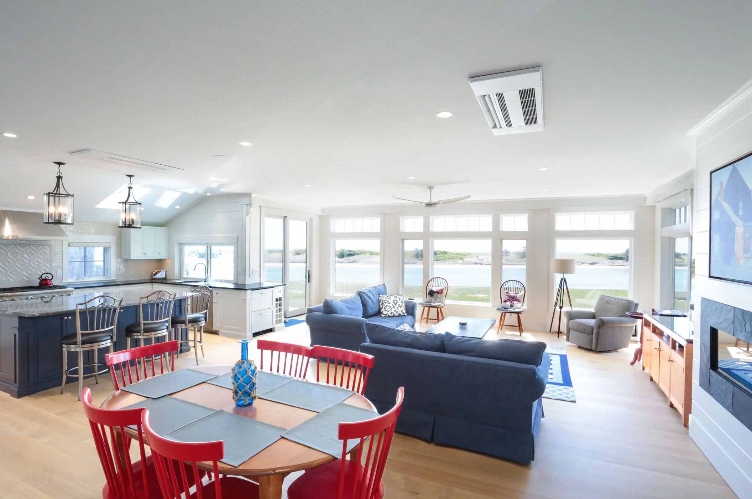 A bright and expansive waterfront living space designed by Lindsey Architects, featuring open-concept coastal interiors, panoramic marsh views, and seamless connections between the kitchen, dining, and living areas. Large windows, soft natural finish
