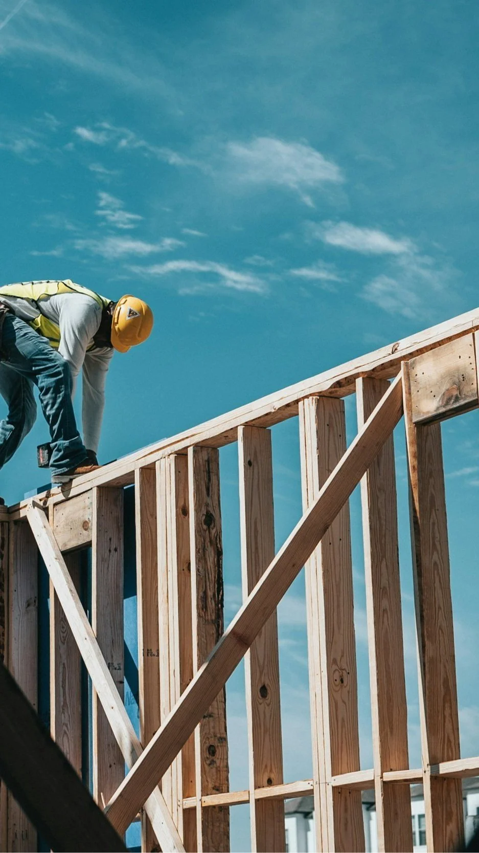 A builder in a hard hat framing a custom home against a blue sky, illustrating the construction process Lindsey Architects guides clients through.