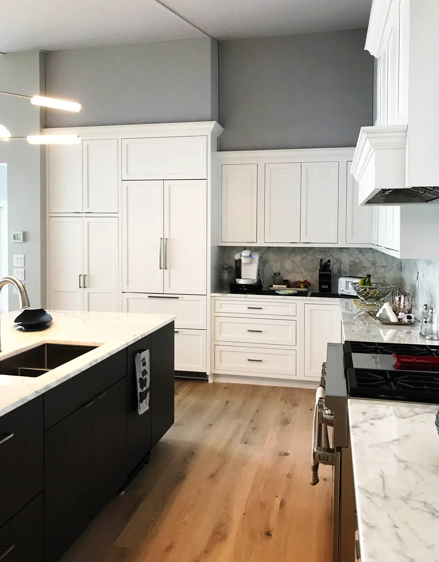 Modern coastal luxury kitchen featuring custom white shaker cabinetry, a dramatic black island with white marble waterfall countertop, integrated panel-ready refrigerator, professional-grade stainless steel range with custom hood, marble slab backspl
