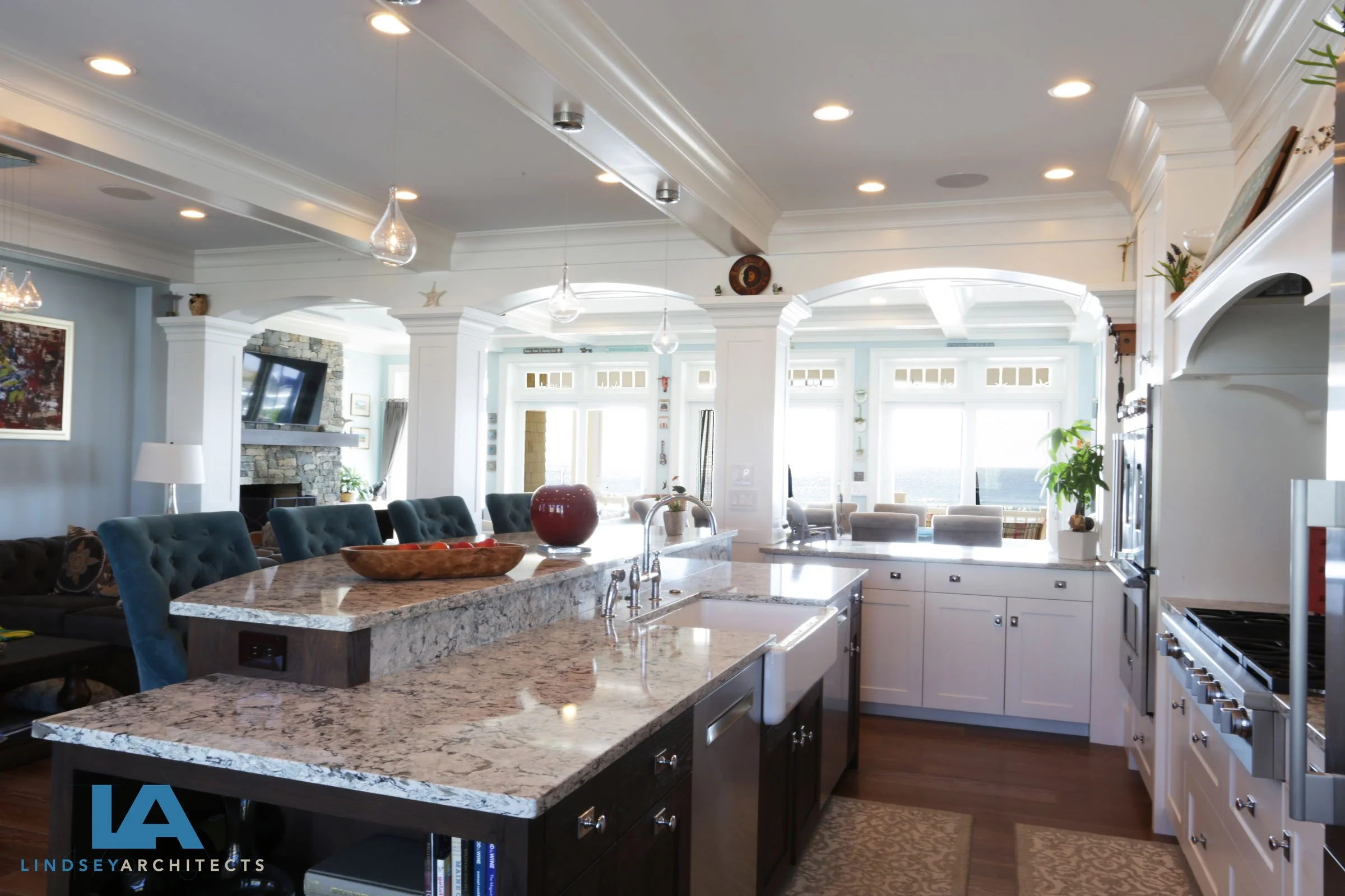 Keyword-Rich Image Description
Coastal luxury open-concept kitchen featuring a large center island with granite countertop and navy blue upholstered counter stools, custom white shaker cabinetry, stainless steel appliances, decorative archway detaili