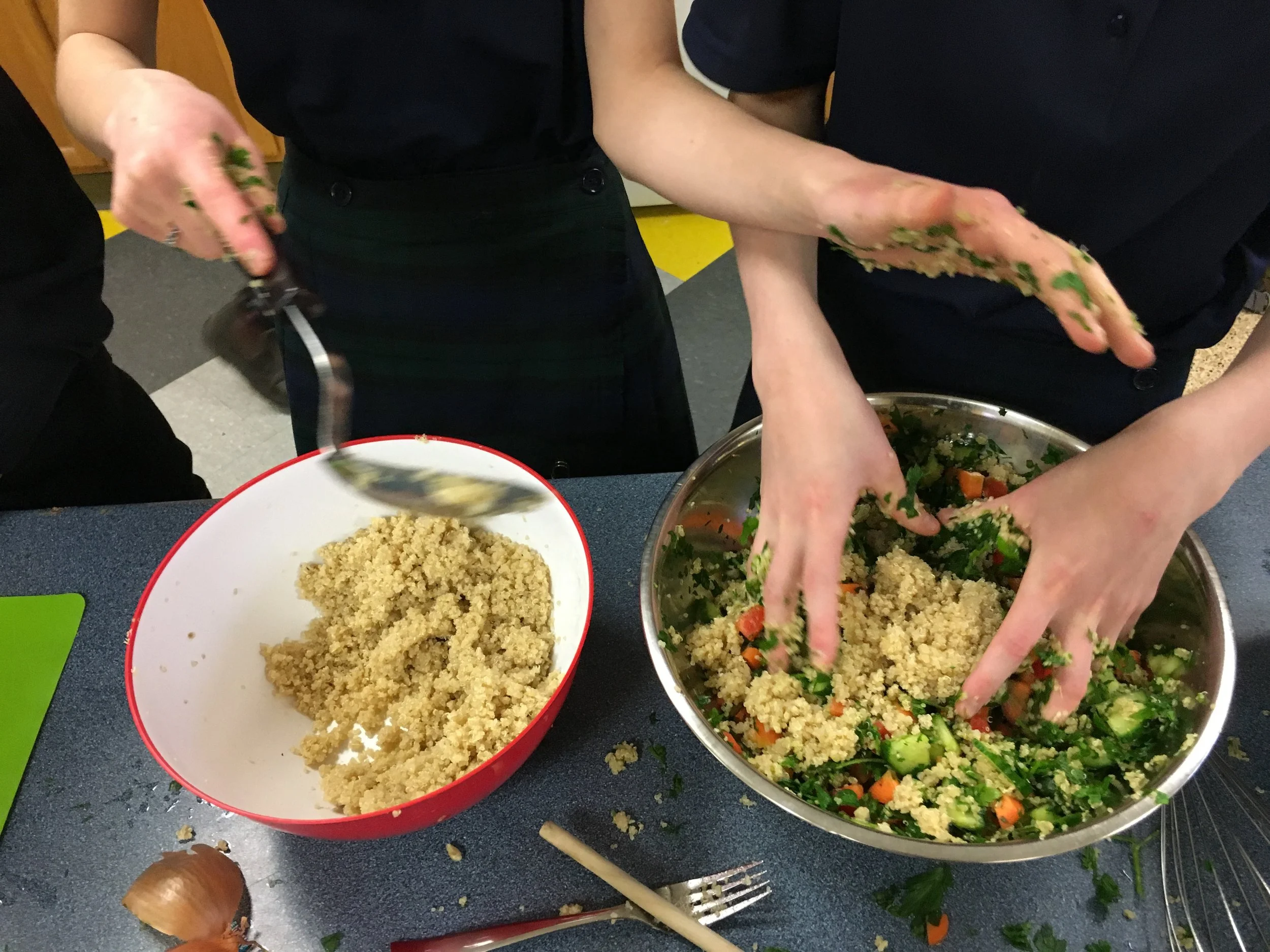 People preparing a vegetable salad with quinoa, cucumbers, carrots, and herbs in a kitchen setting.