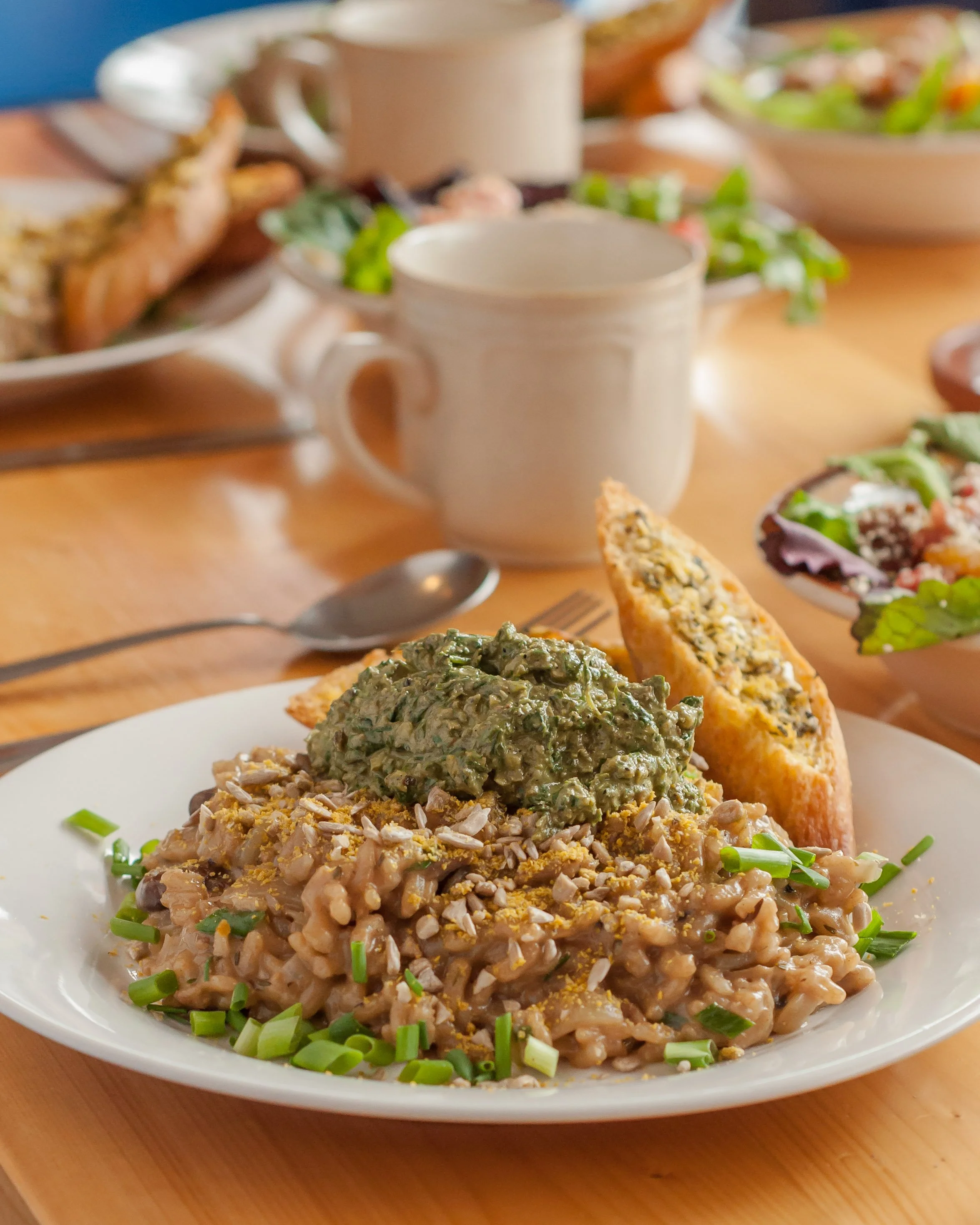 Plate of lentil dish topped with chopped green onions, served with two slices of garlic bread, on a wooden table with mugs and other dishes in the background.