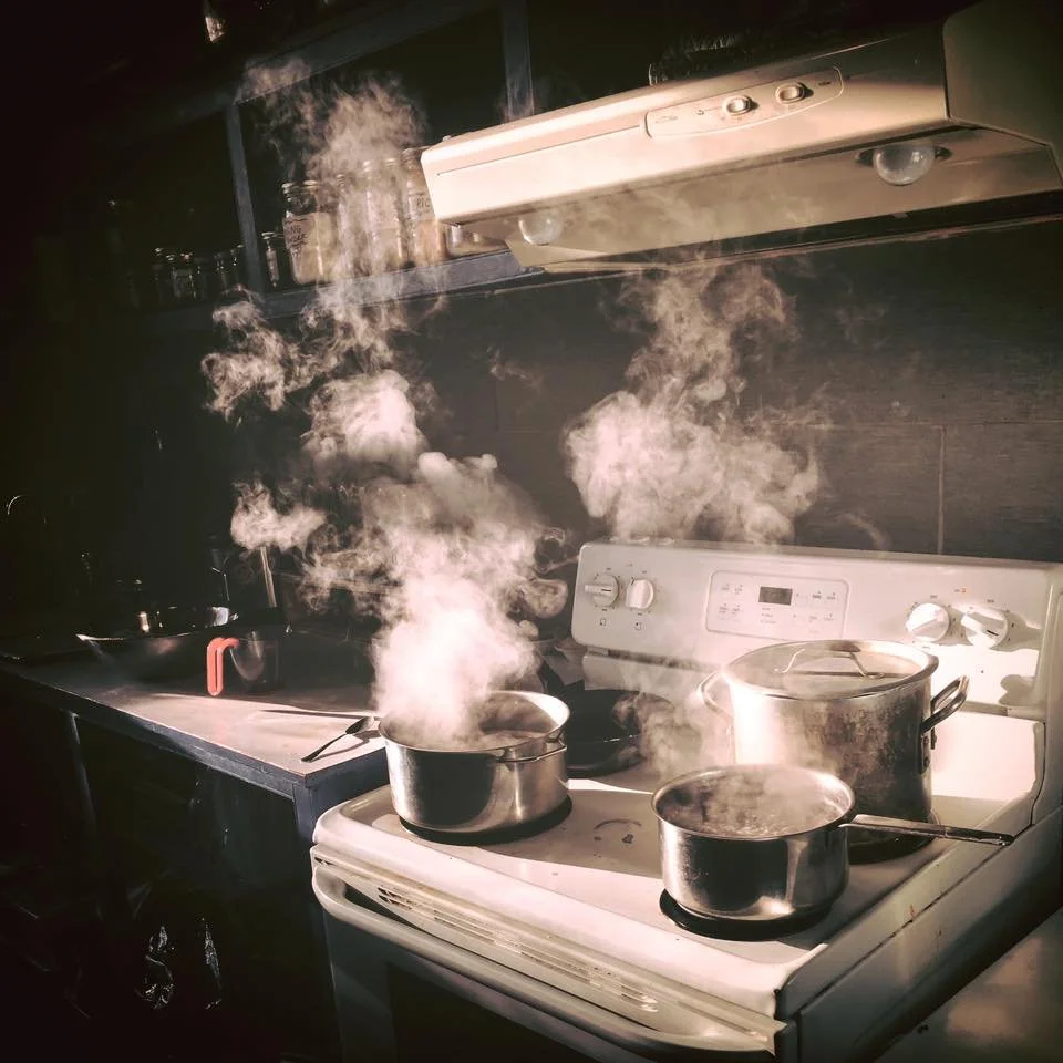 Several pots on a stove with steam and smoke rising from them, in a kitchen setting.