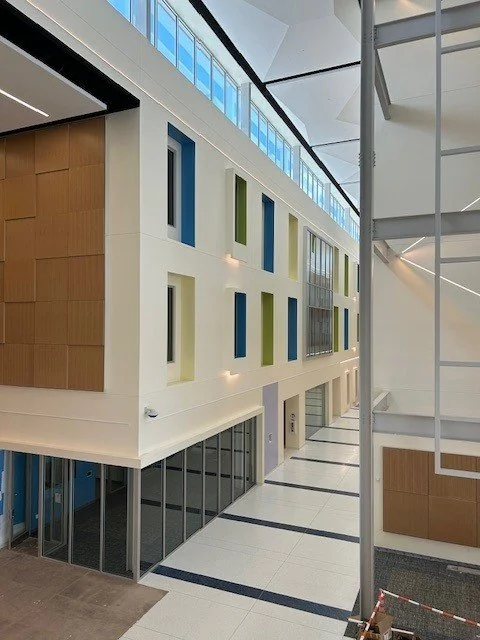 Interior of a modern building with a high ceiling, large windows, colorful rectangular wall accents, and a glass-walled corridor.