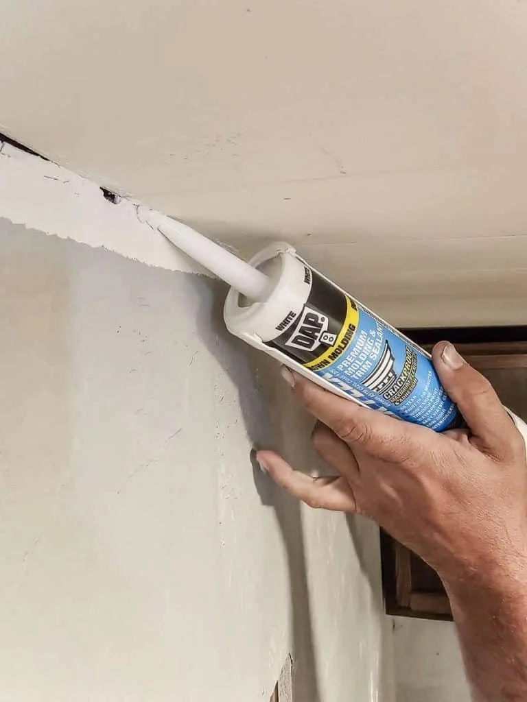A person applying caulk with a caulk gun to a corner of a wall and ceiling during home renovation.