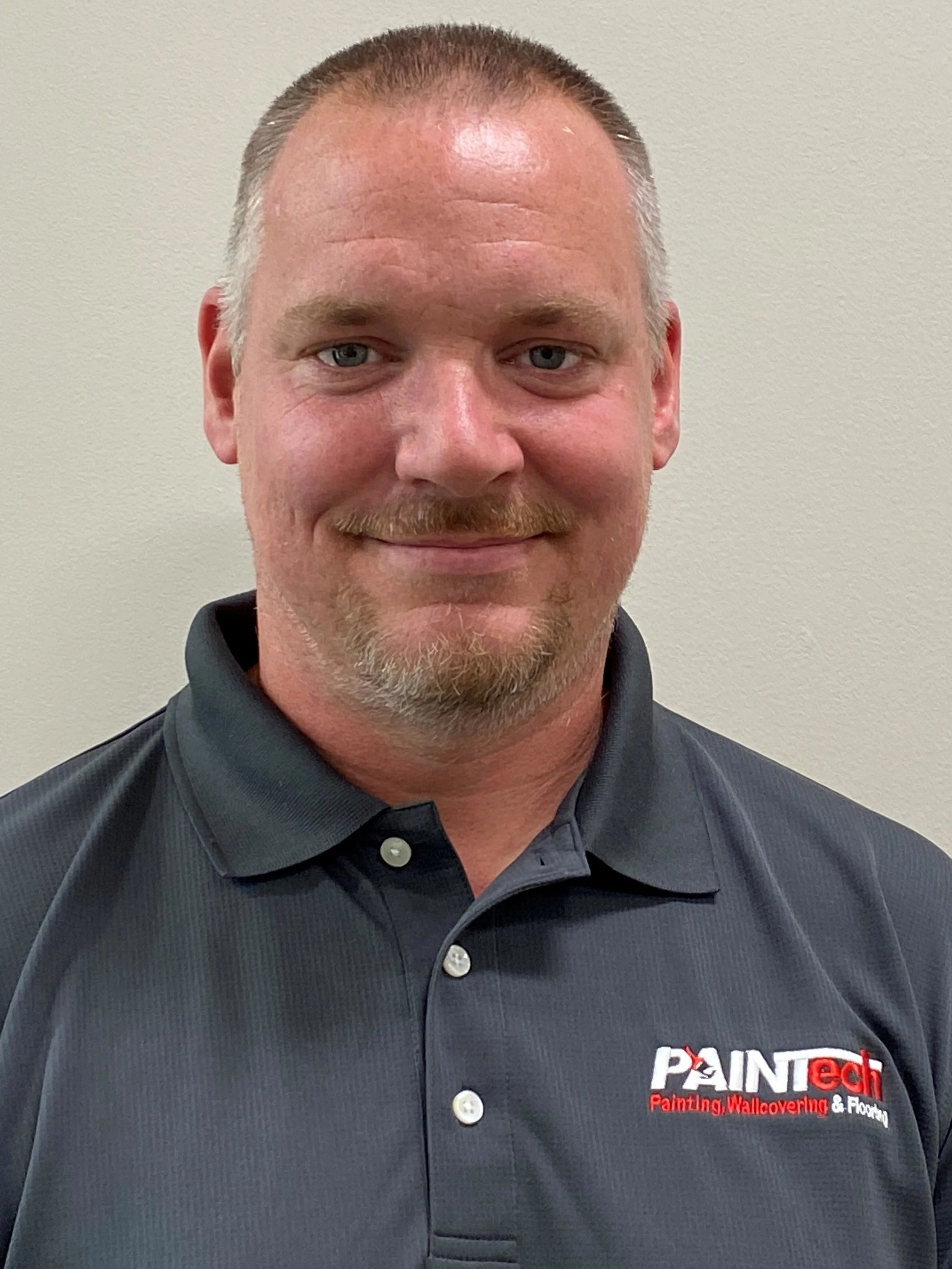 Close-up of a man wearing a black polo shirt with a logo that reads 'Painted Wallcovering & Flooring'.