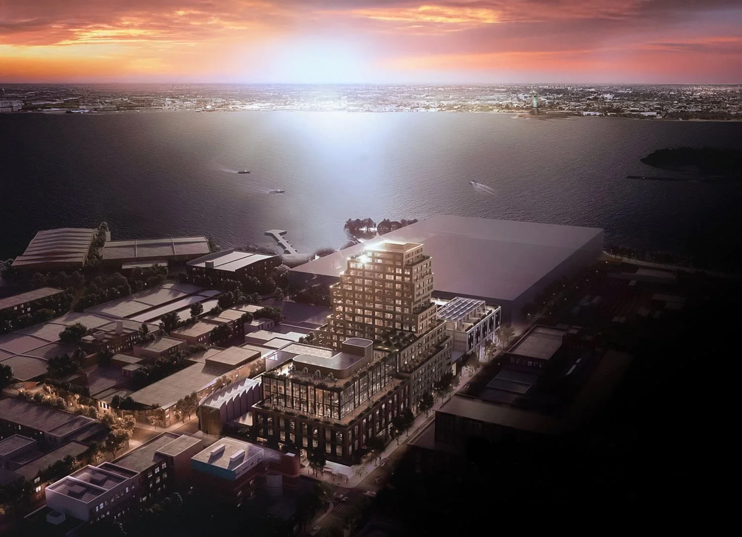 Aerial view of a modern urban waterfront area at sunset, featuring a prominent multi-story building with terraces and surrounding industrial structures. The water and city skyline are visible in the background.