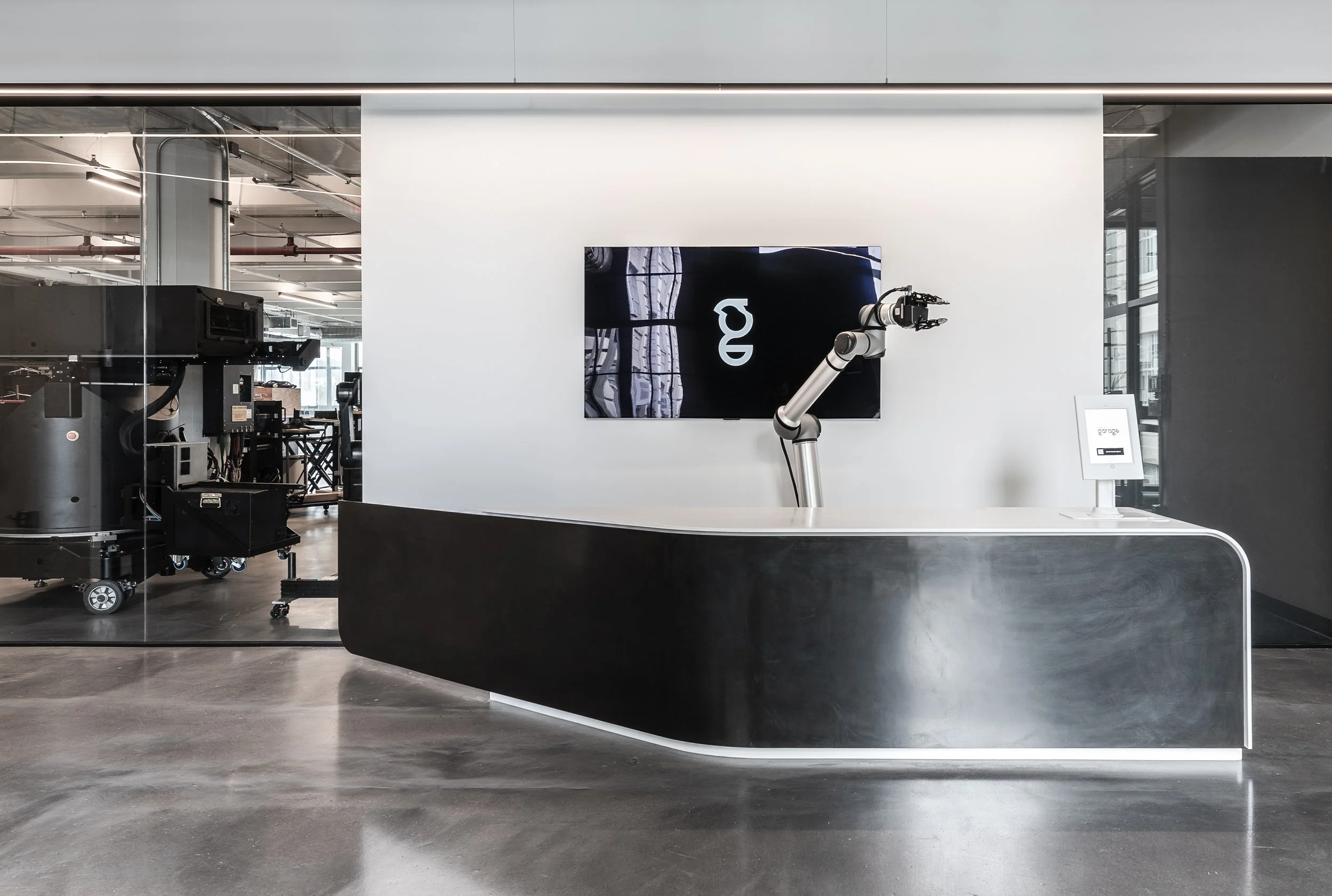 Modern reception desk with robotic arm and industrial machinery in the background, digital display on wall, minimalistic design.