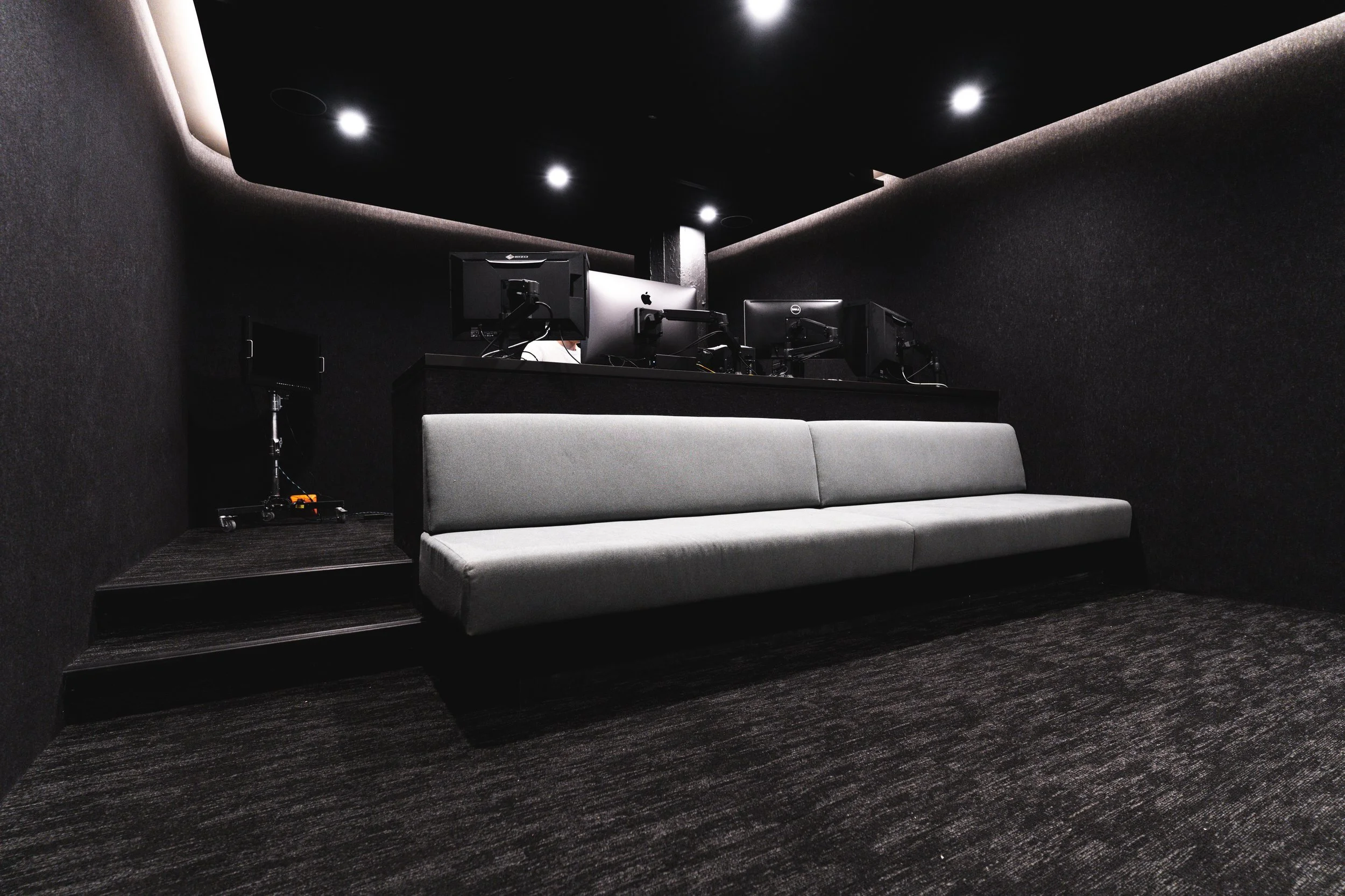 Dark computer room with a gray sofa and several computer monitors on a raised platform.