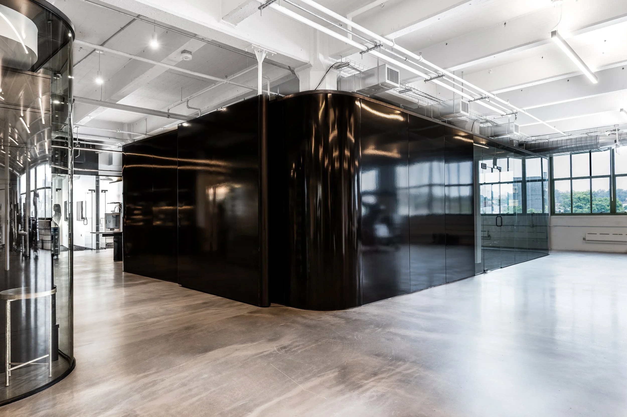 Modern industrial office space with large black curved wall, glass dividers, and concrete floor.