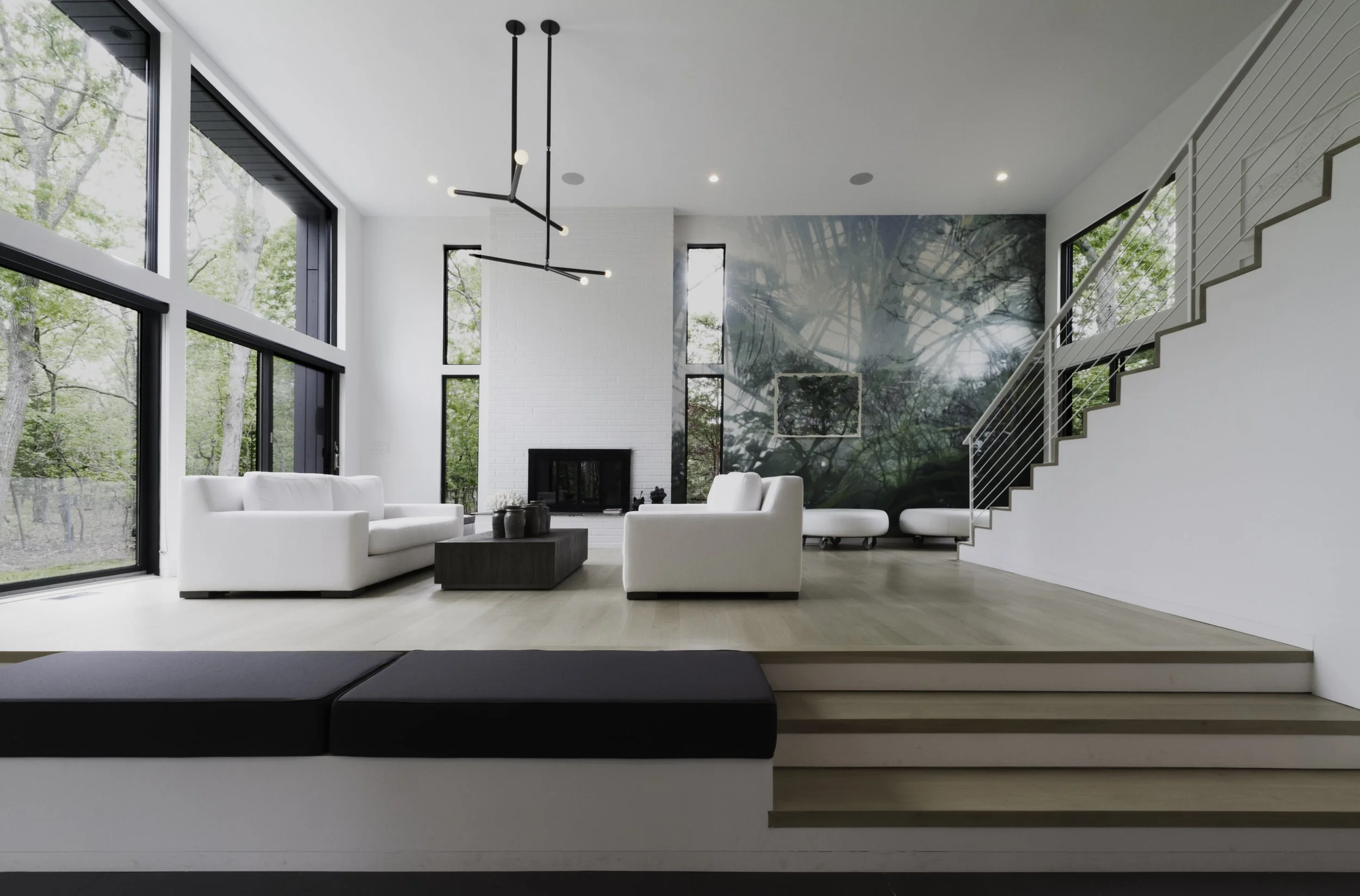 Modern living room with large windows, white furniture, minimalist decor, and a staircase.