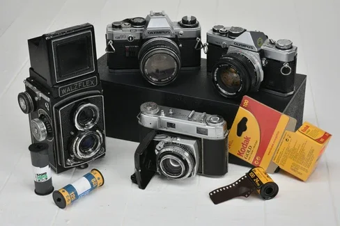 Collection of vintage cameras, film rolls, and Kodak flashcubes displayed on a white surface.