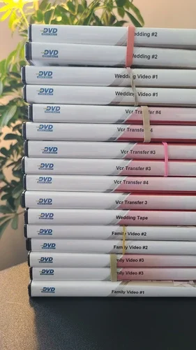Stack of home-recorded DVDs labeled with family video titles including wedding videos and VCR transfers, ready for DVD to digital conversion.