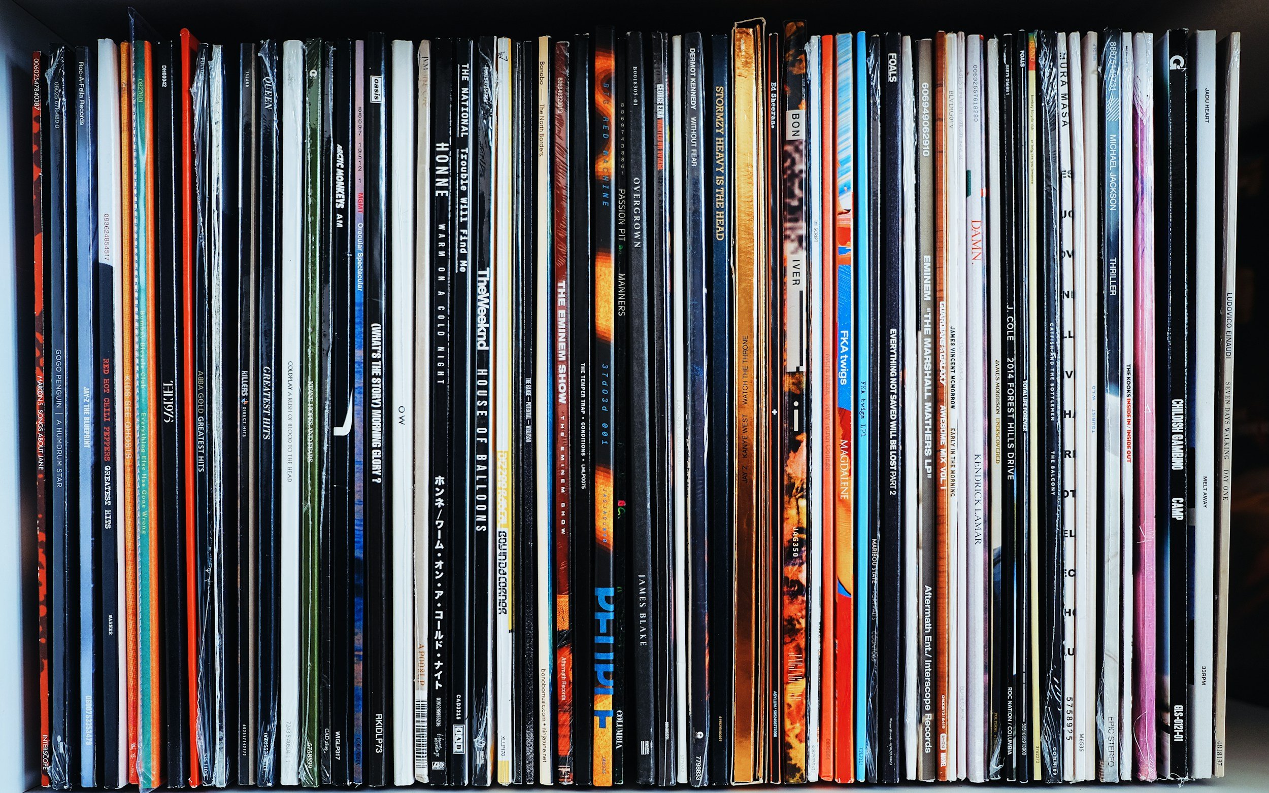 A collection of vertically stacked vinyl records with visible titles on their spines, including genres like music, movies, and other media.