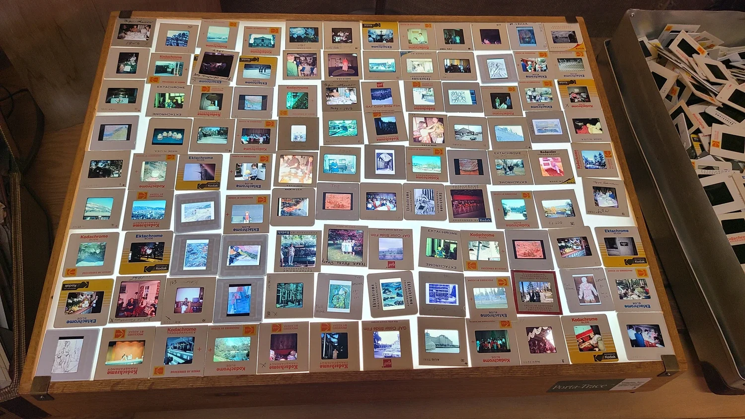 A collection of vintage photo slides and film negatives laid out on a wooden table, with some slides stacked on enclosed trays and others scattered around.