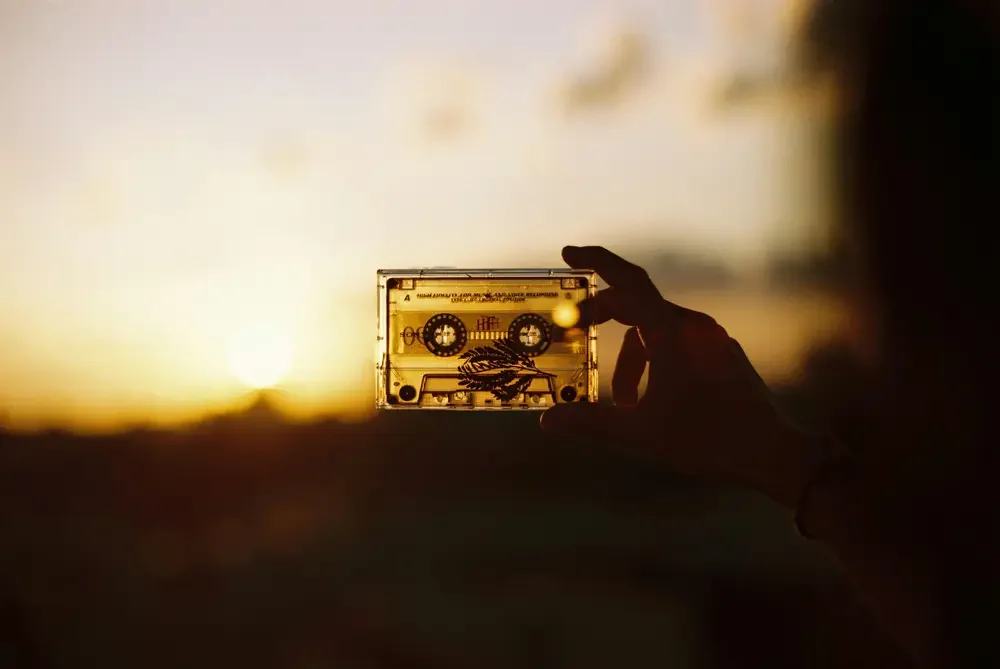 Person holding a cassette tape against a sunset sky.