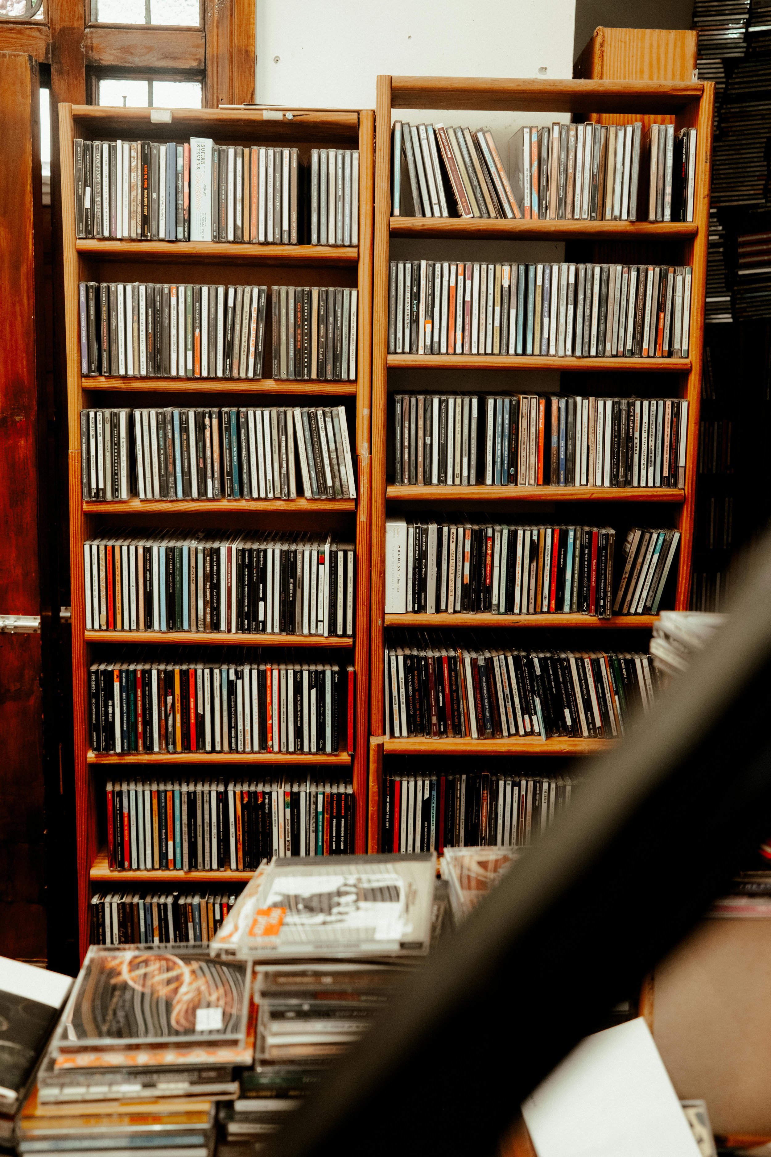 Wooden shelves filled with CDs in cases, with a stack of CDs on a table in the foreground.