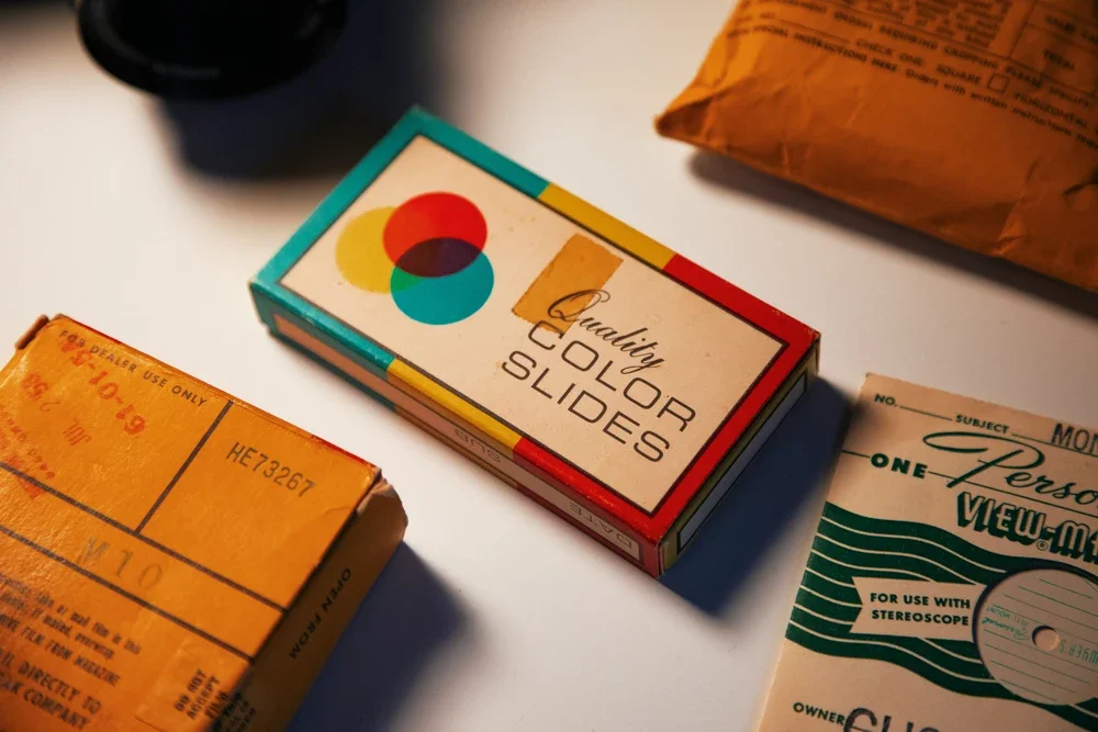Assorted vintage slide film boxes on a white surface, with one box labeled "Color Slides" featuring a colorful circle design.