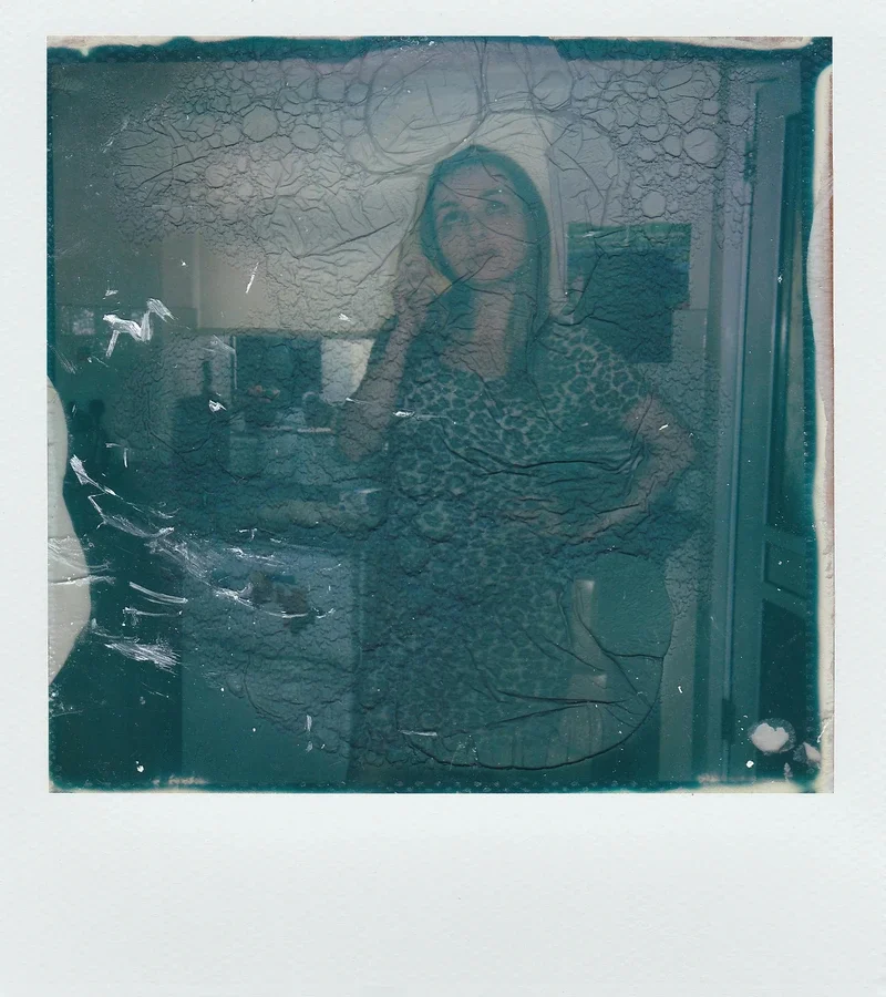 A woman wearing a leopard print top is taking a selfie in a cracked and dirty mirror.