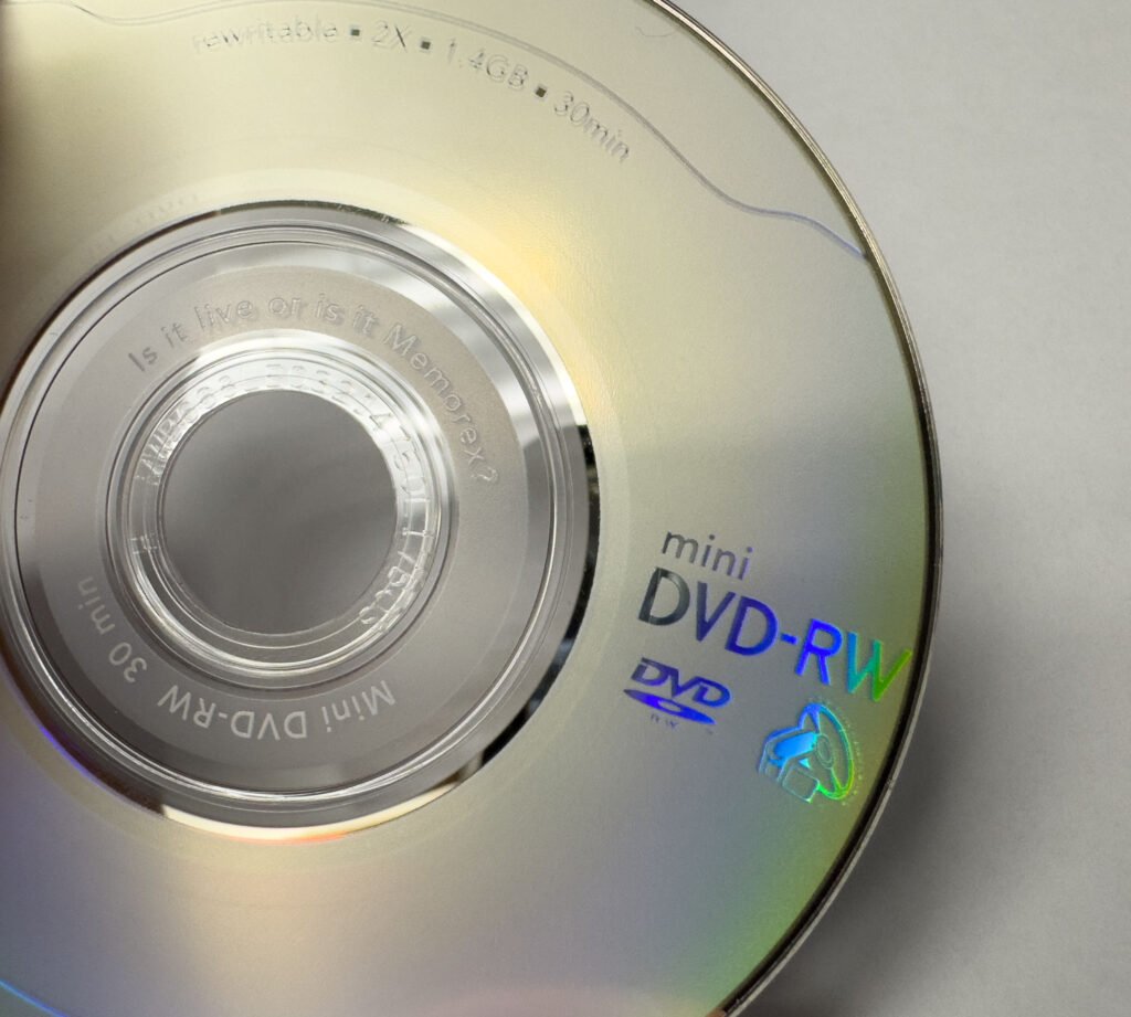 A close-up of a mini DVD-RW disc with reflective silver surface, labeled with blue and green holographic text, and notes about the disc's specifications.
