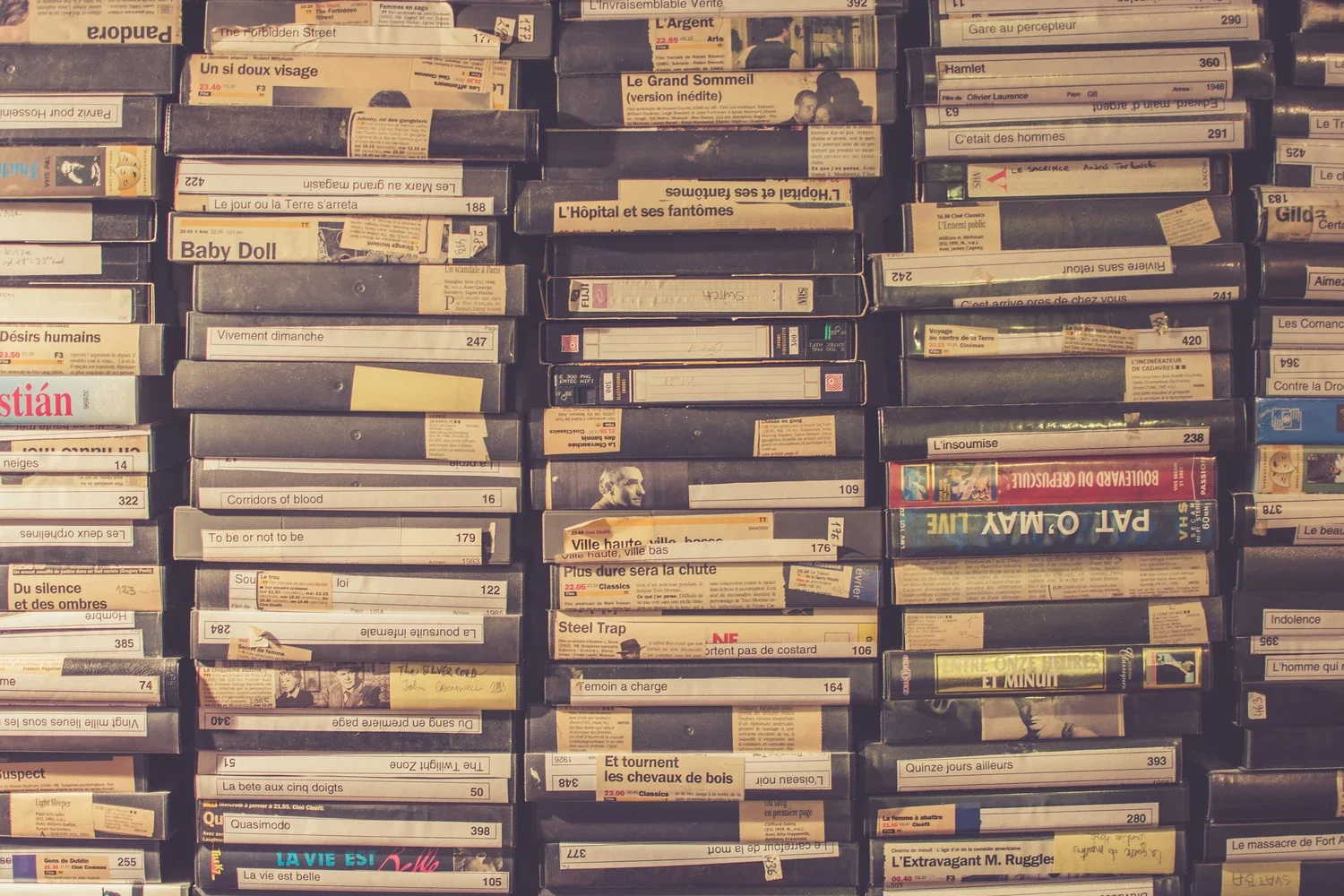 View of tightly packed VHS tapes on shelves, with many labels and handwritten notes, mostly in French and English.