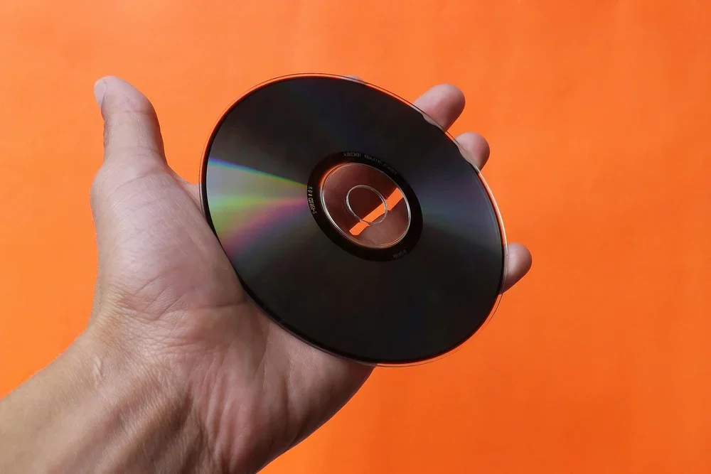 A hand holding a black CD against an orange background.