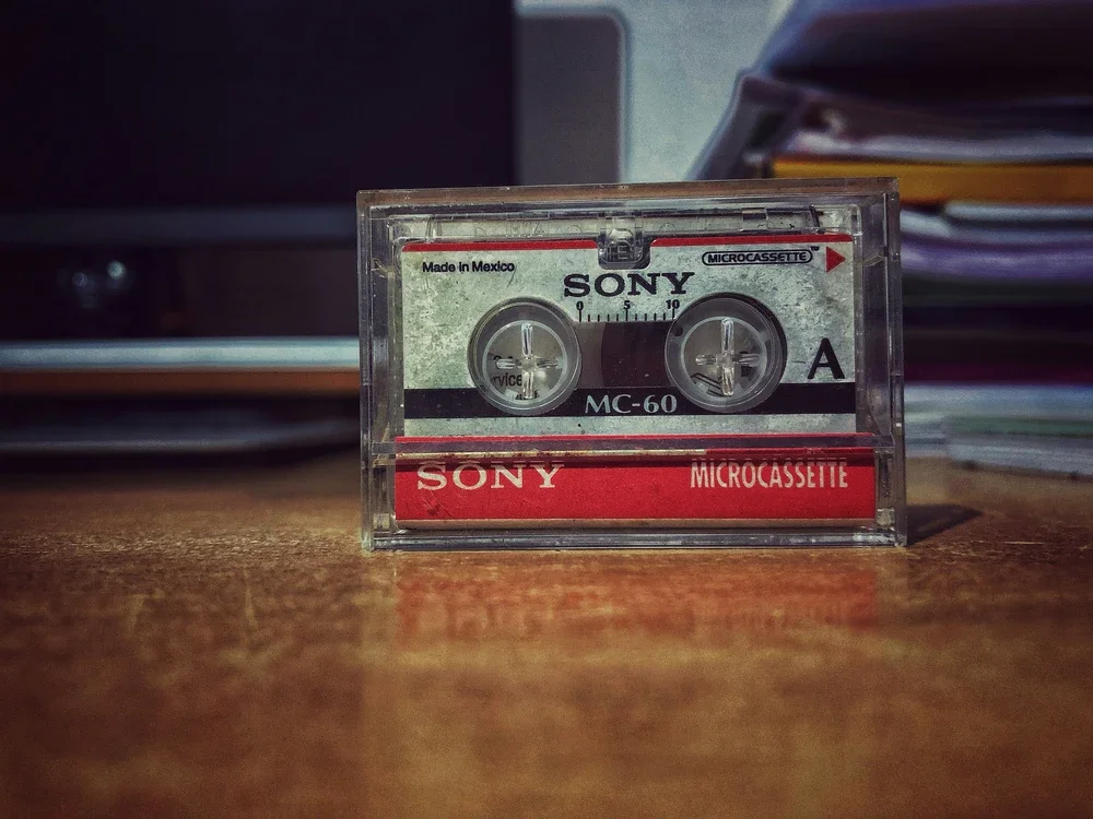 Close-up of a vintage Sony microcassette tape recorder labeled 'Microcassette' and 'Sony' on a wooden desk