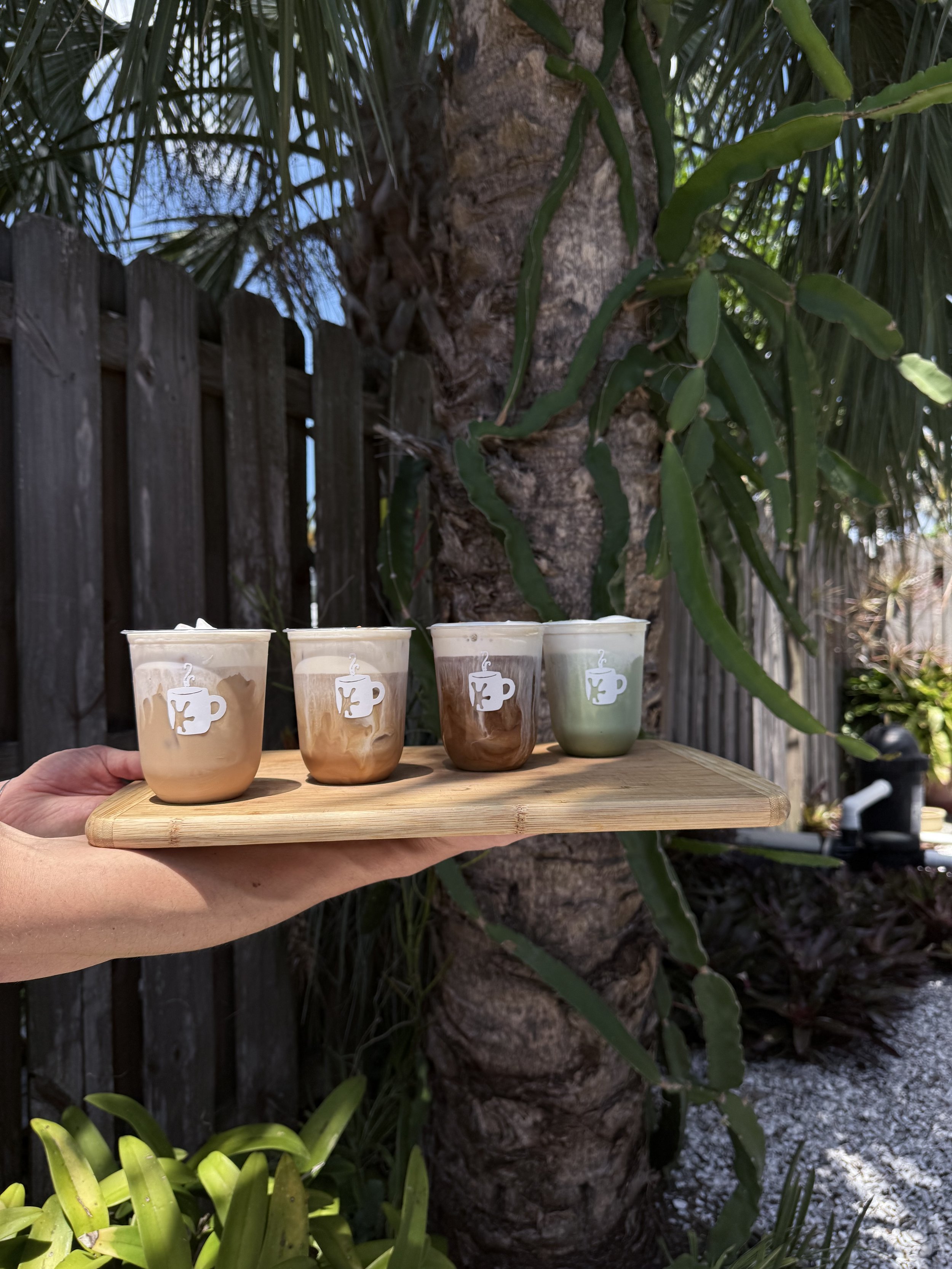 Three handcrafted espresso drinks and one matcha latte from Greenhaus Coffee Co served on a board.