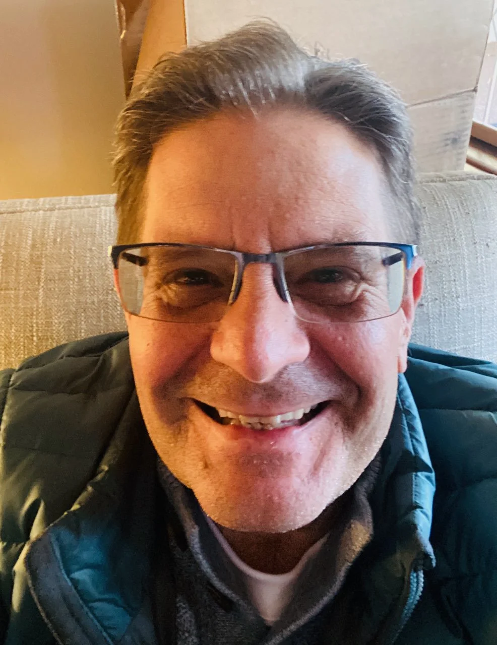 Close-up of smiling man with glasses sitting on a sofa.