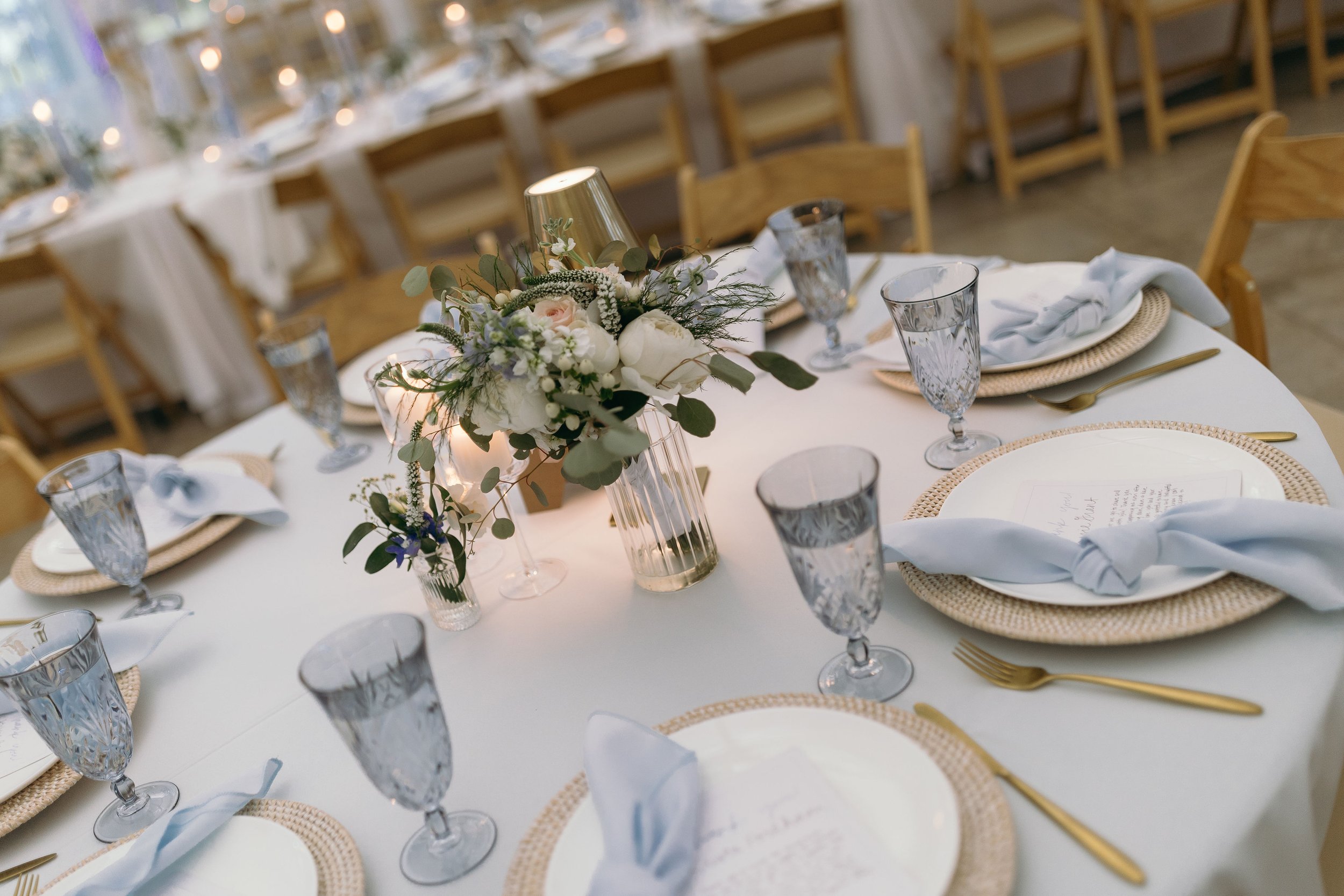Elegant table setting with white tablecloth, floral centerpiece, gold cutlery, crystal glasses, and light blue napkins.