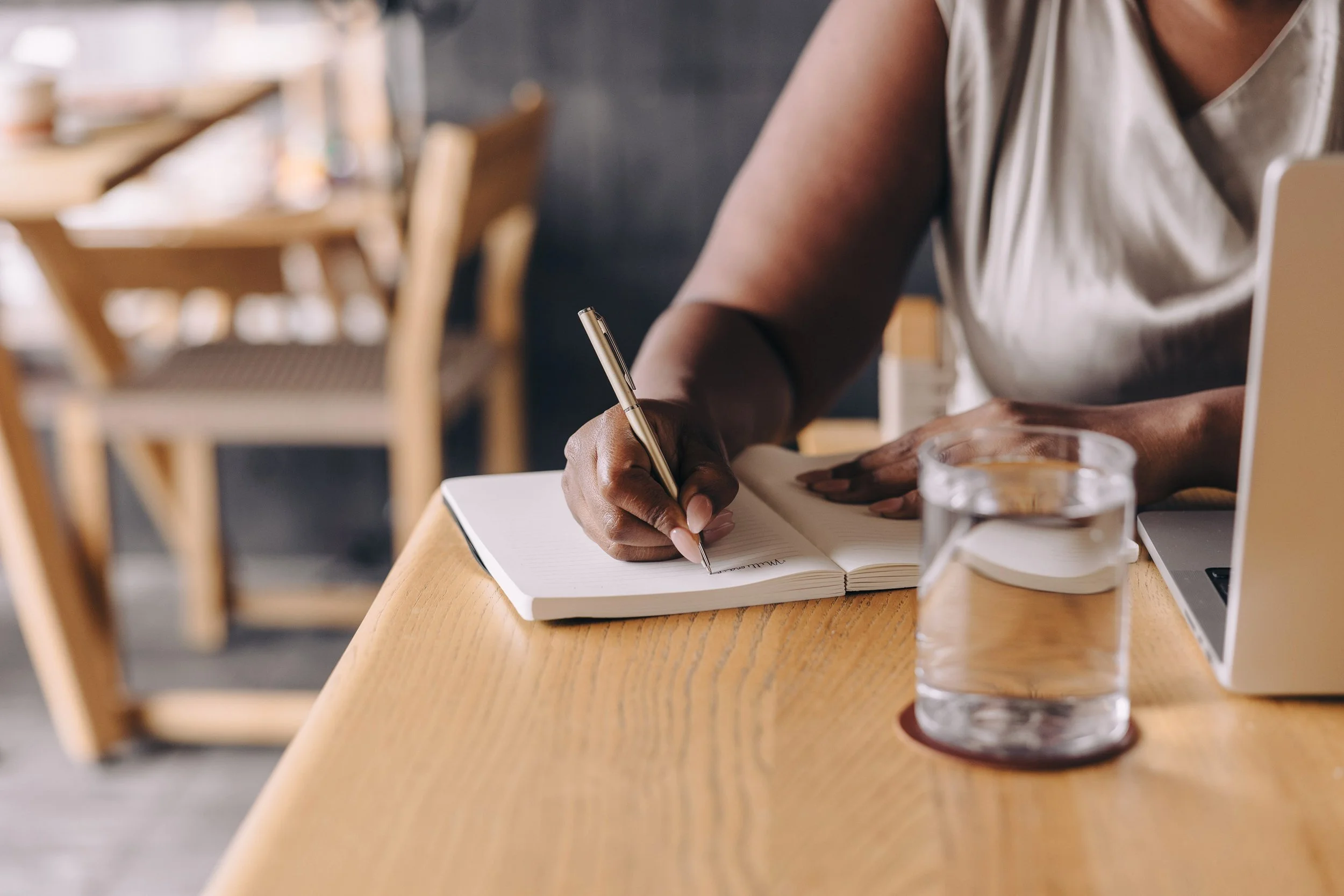 A woman sitting at a table writing in a notebook.