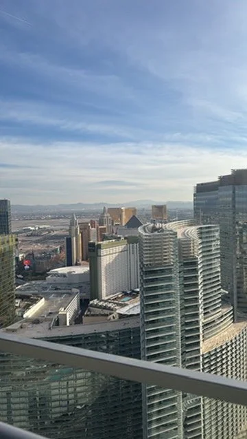 Cityscape with tall buildings under a partly cloudy sky, viewed from a high-rise balcony.