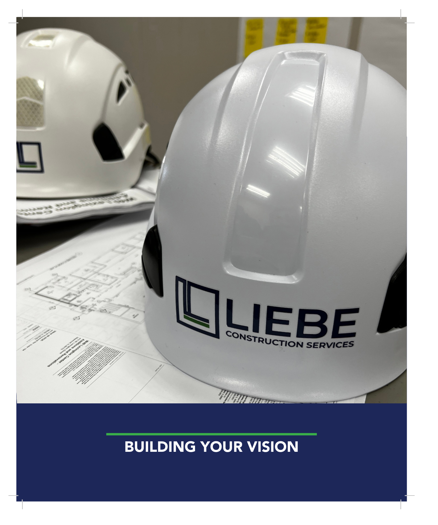 Close-up of a white construction helmet with the logo of Lieb Construction Services, placed on top of architectural plans and blueprints on a table.